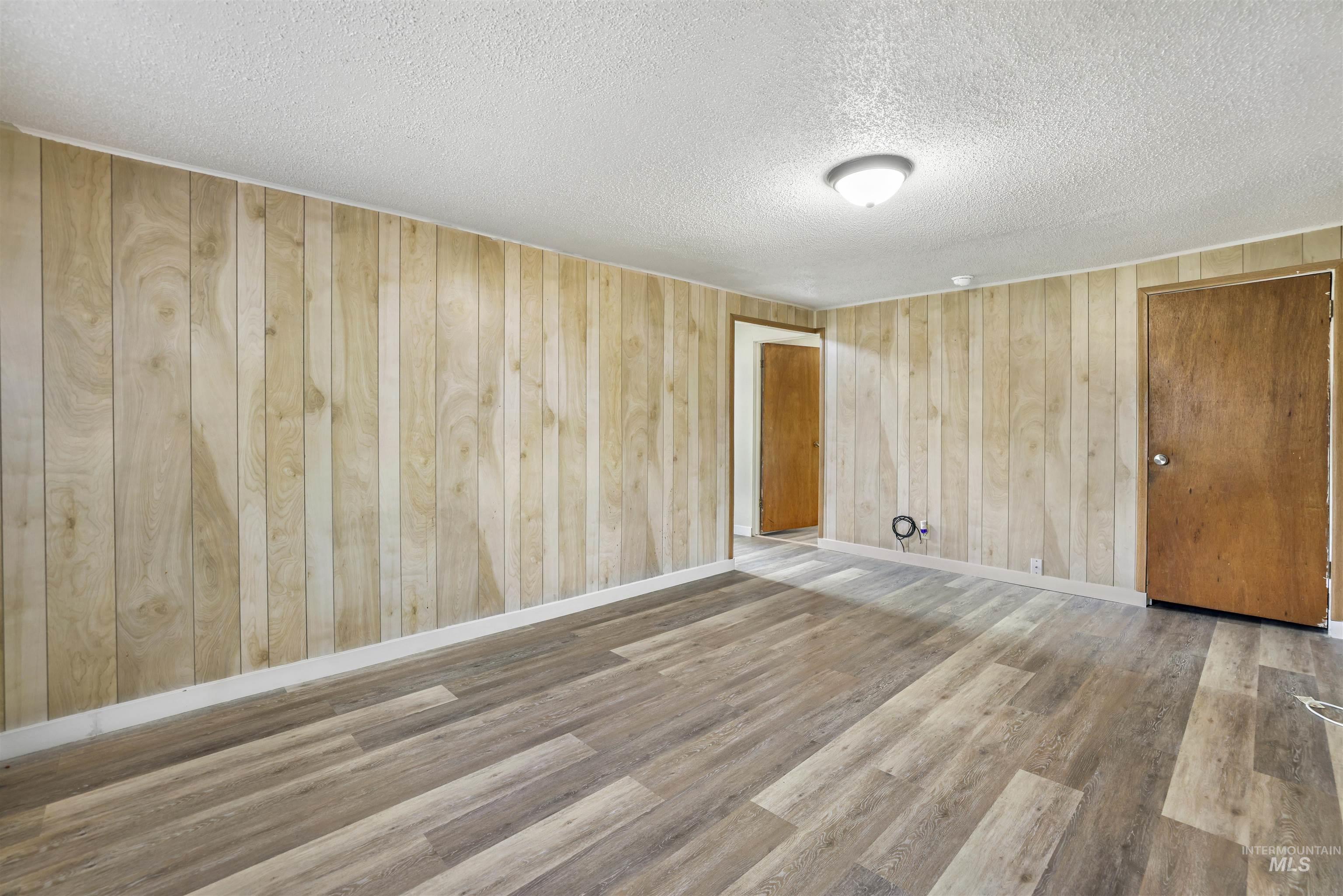 Unfurnished room featuring wood walls, light wood-style floors, and a textured ceiling