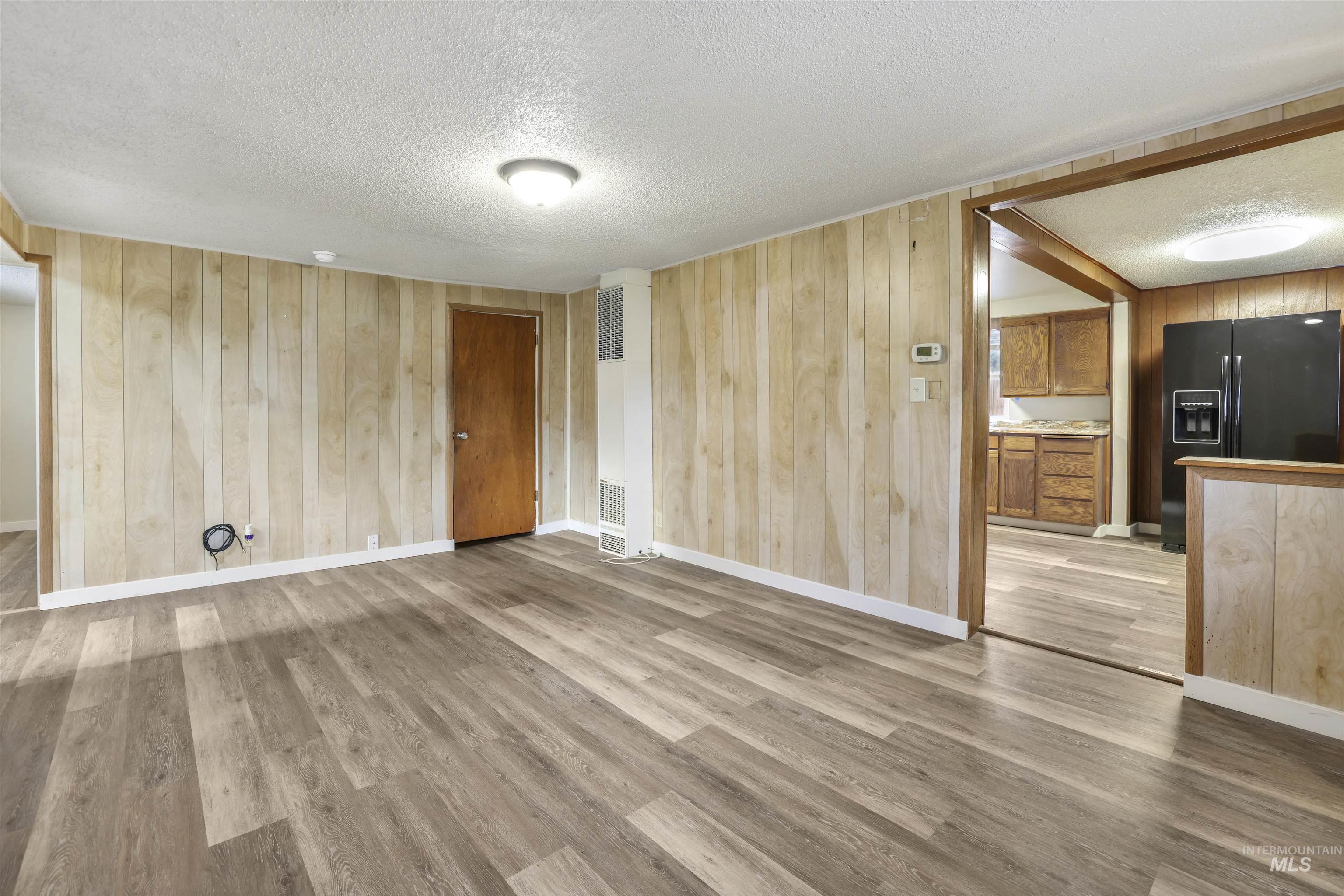 Unfurnished living room with wood walls, a textured ceiling, light wood-style flooring, and a heating unit
