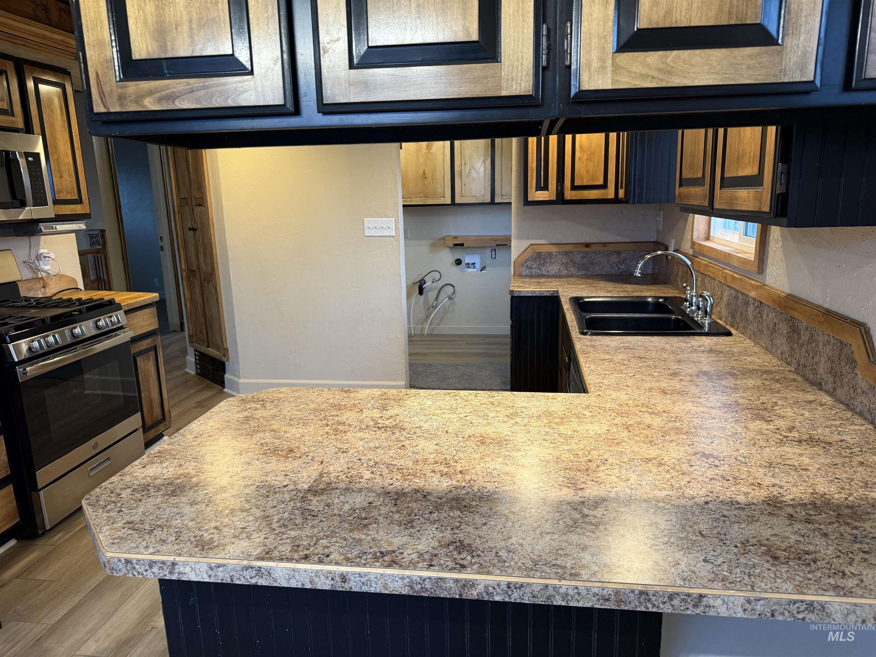 Kitchen featuring stainless steel appliances, a peninsula, light wood-style floors, and light countertops
