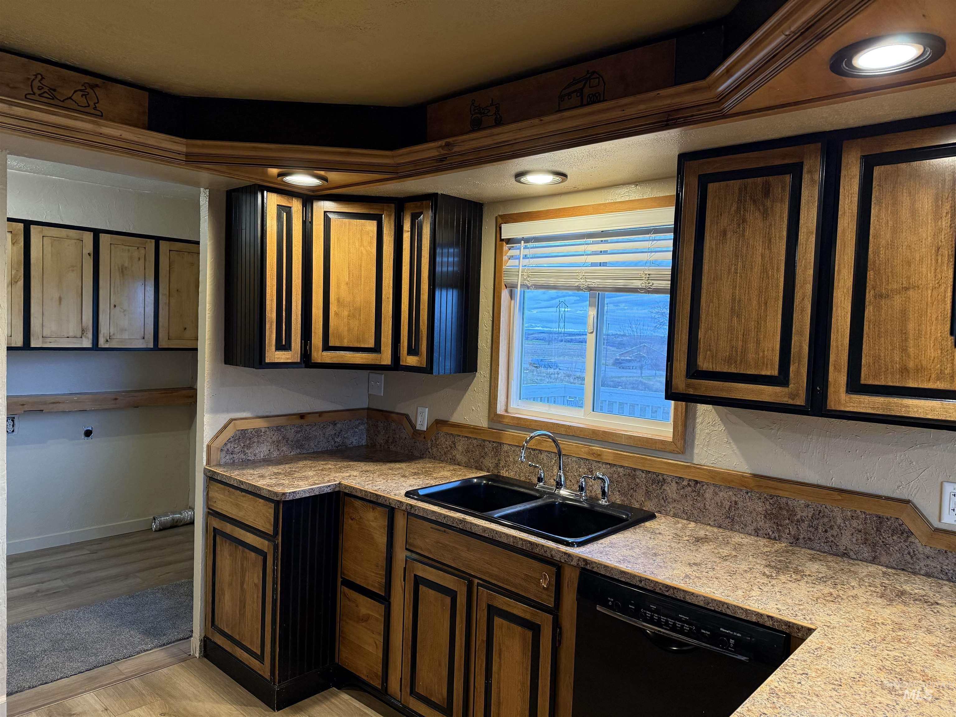 Kitchen with black dishwasher, light wood-style flooring, and light stone countertops