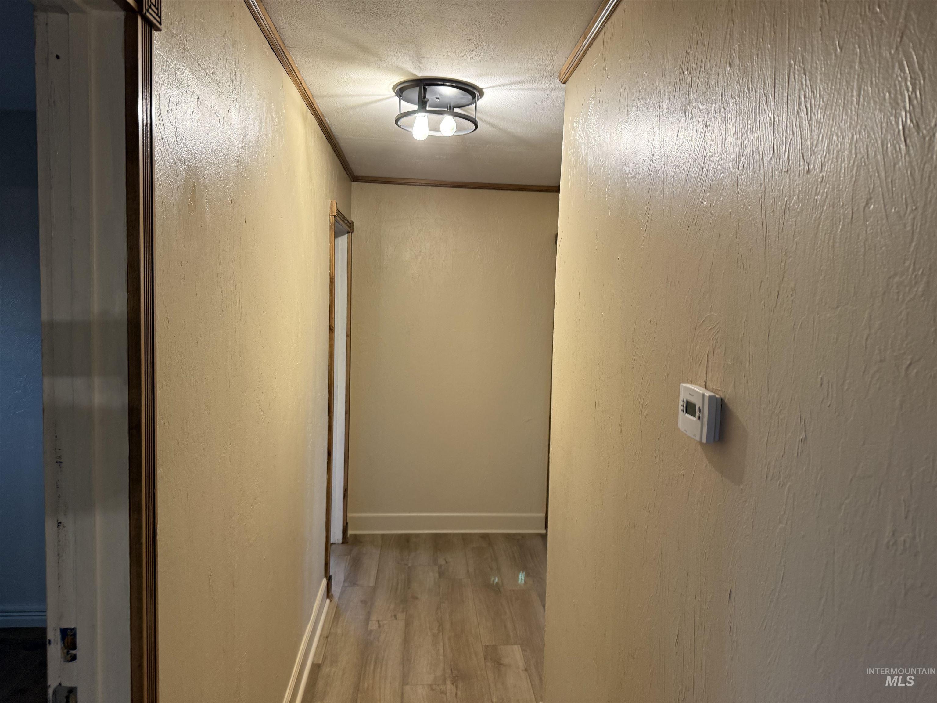 Hall with a textured wall, light wood-style flooring, and crown molding