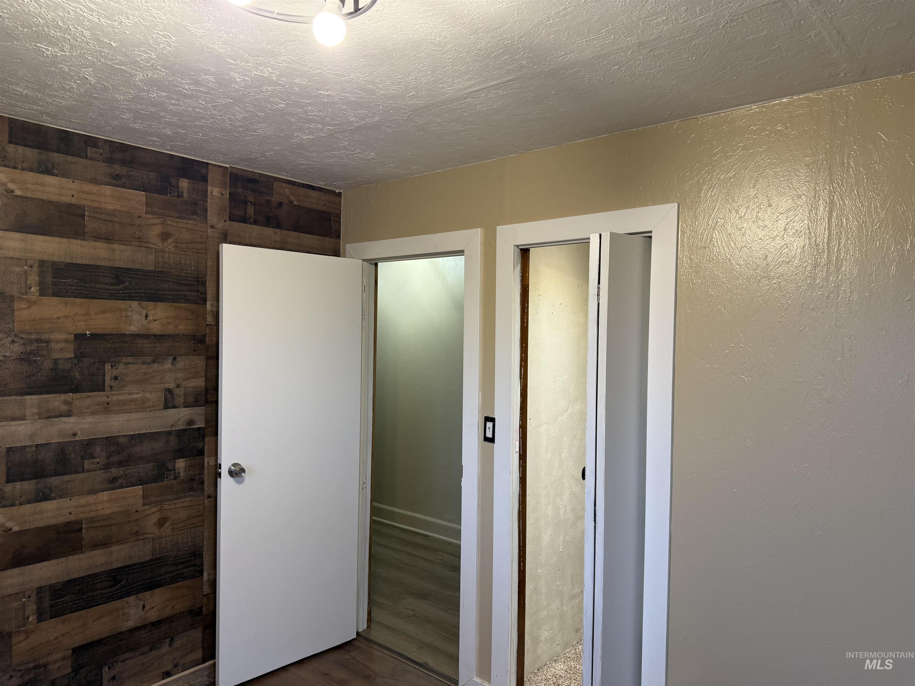 Unfurnished bedroom with wood finished floors, wooden walls, and a textured ceiling