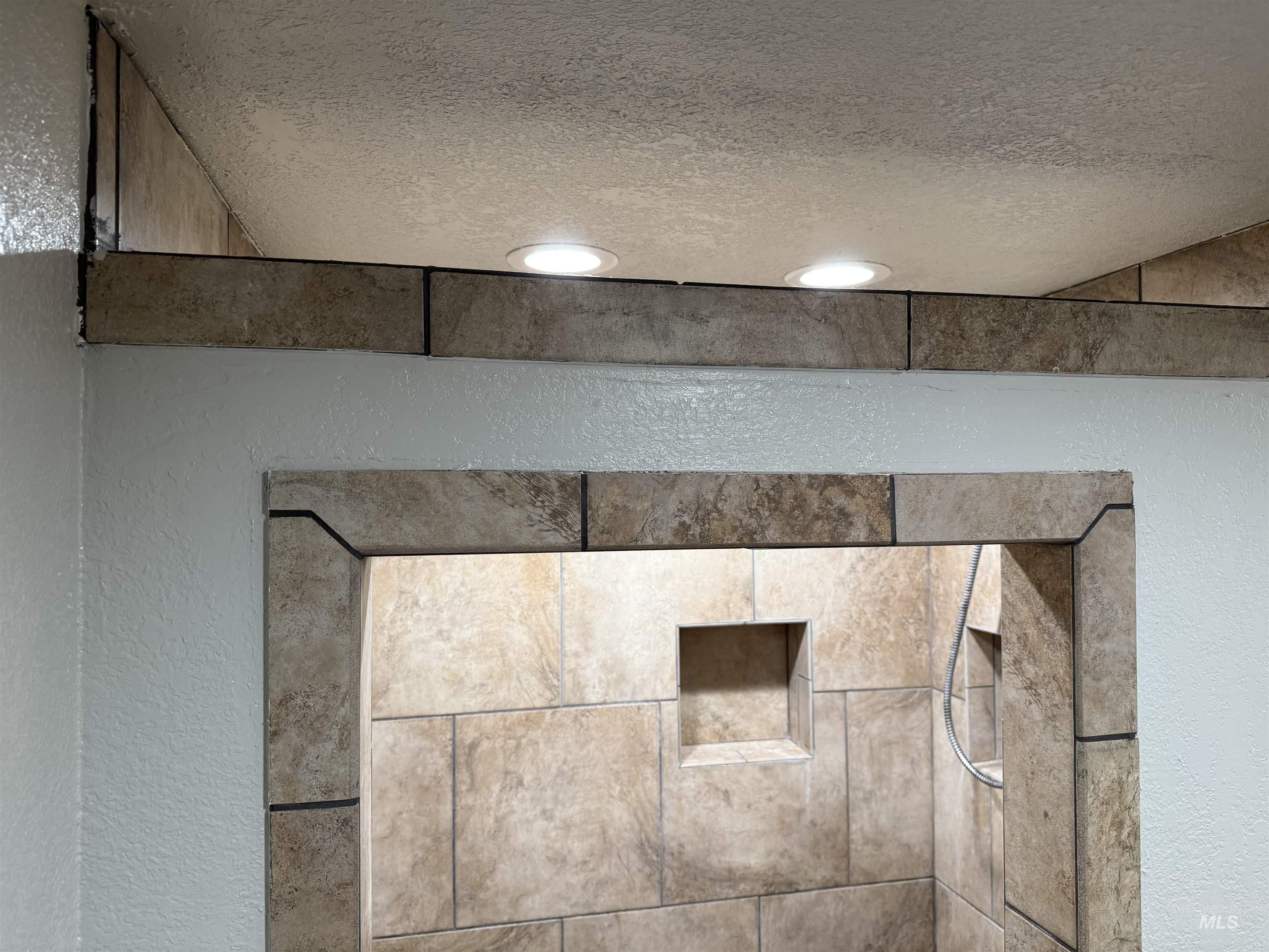 Bathroom view of a textured wall, a shower stall, and a textured ceiling