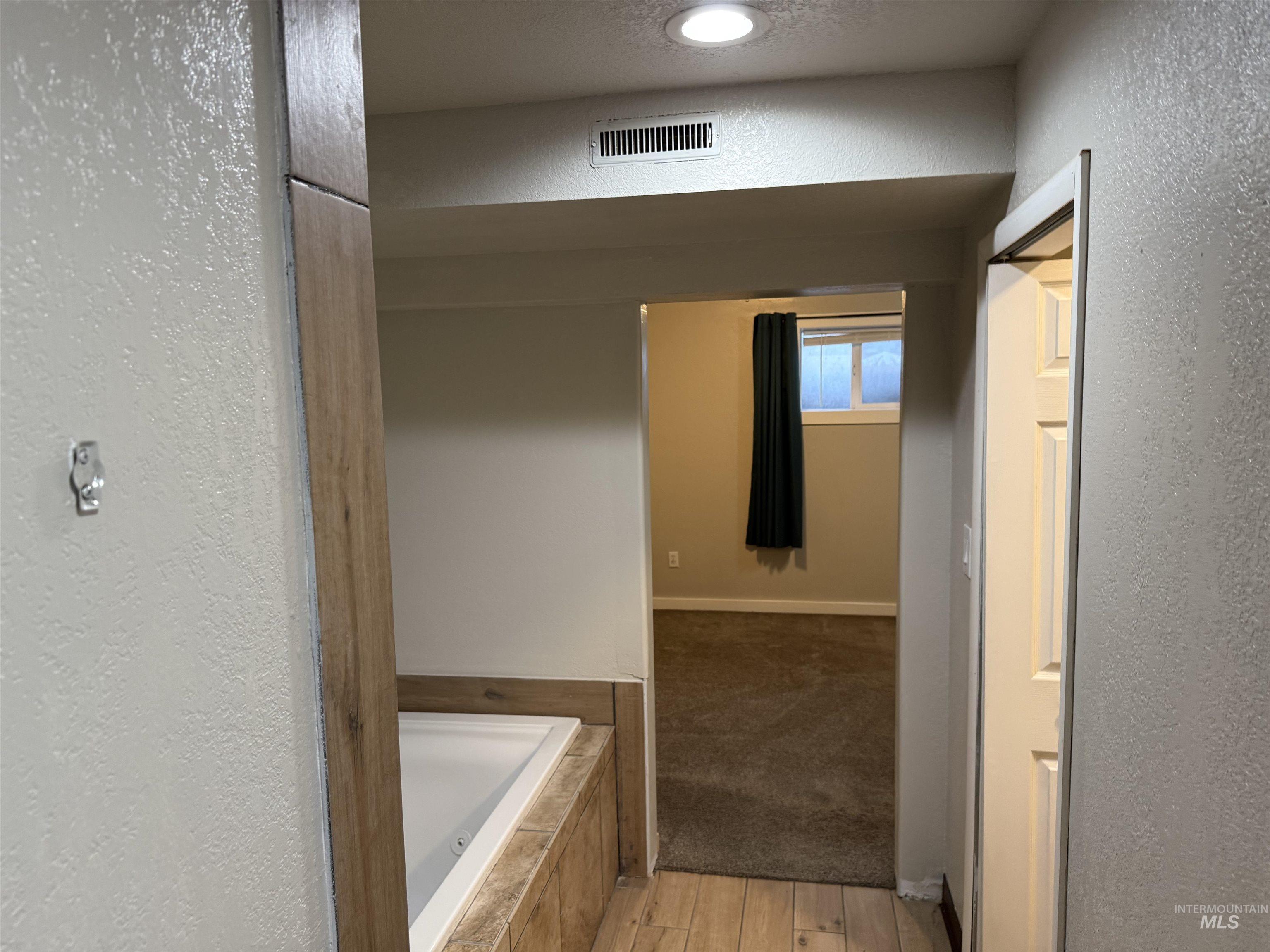 Full bath with a textured wall, tiled tub, and light wood-type flooring