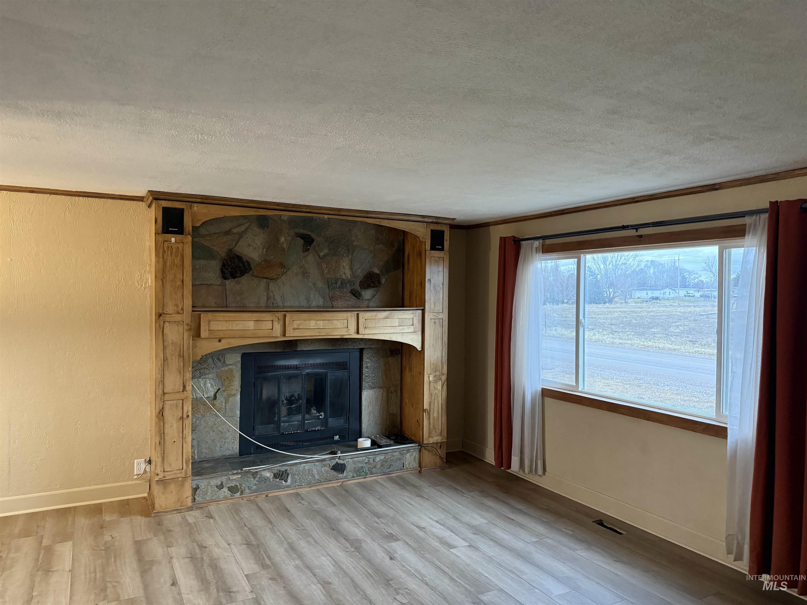 Unfurnished living room featuring a textured ceiling, a fireplace, wood finished floors, ornamental molding, and a textured wall
