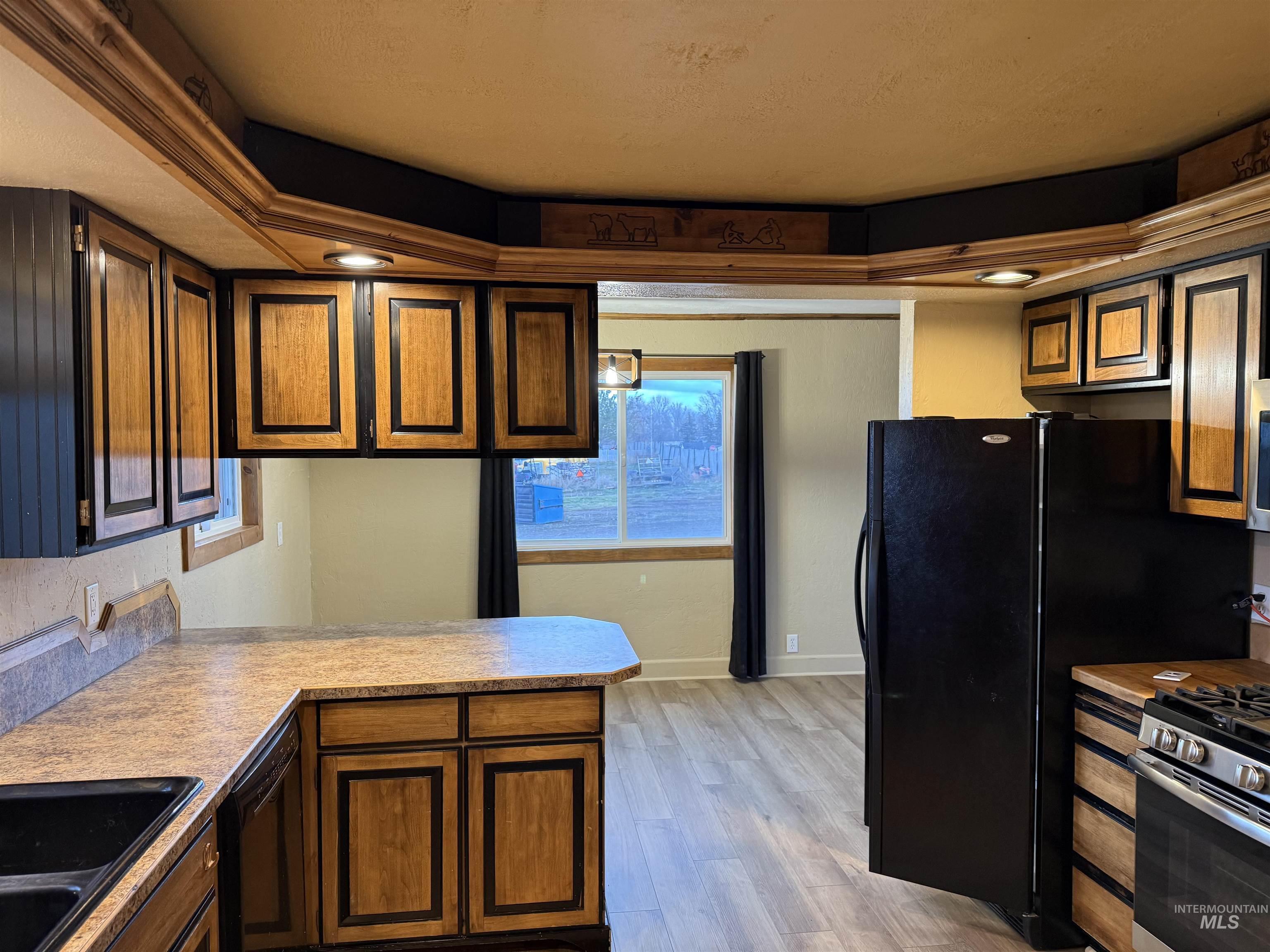Kitchen with stainless steel gas stove, light wood finished floors, light countertops, and a peninsula
