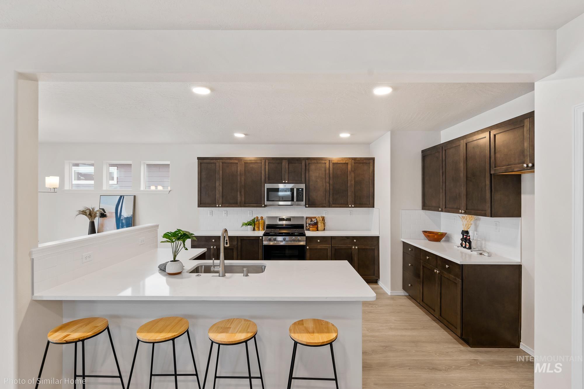Kitchen with dark brown cabinets, a peninsula, stainless steel appliances, a breakfast bar area, and recessed lighting