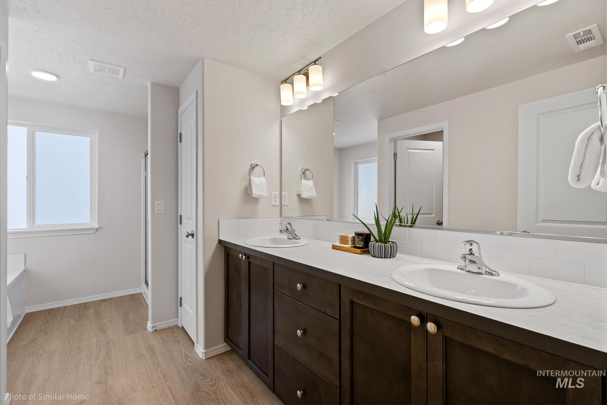 Bathroom featuring double vanity, light wood finished floors, a tub, plenty of natural light, and a textured ceiling