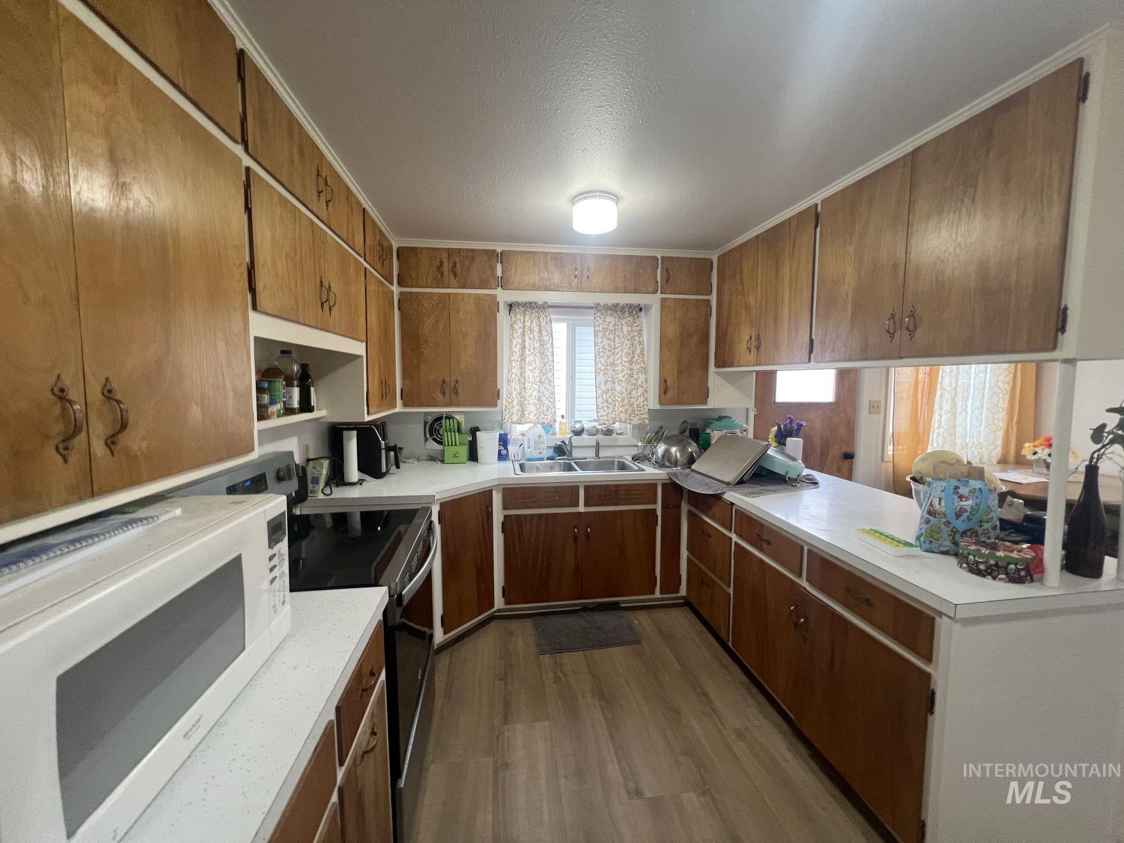 Kitchen featuring white appliances, light countertops, dark wood-style floors, brown cabinetry, and a textured ceiling