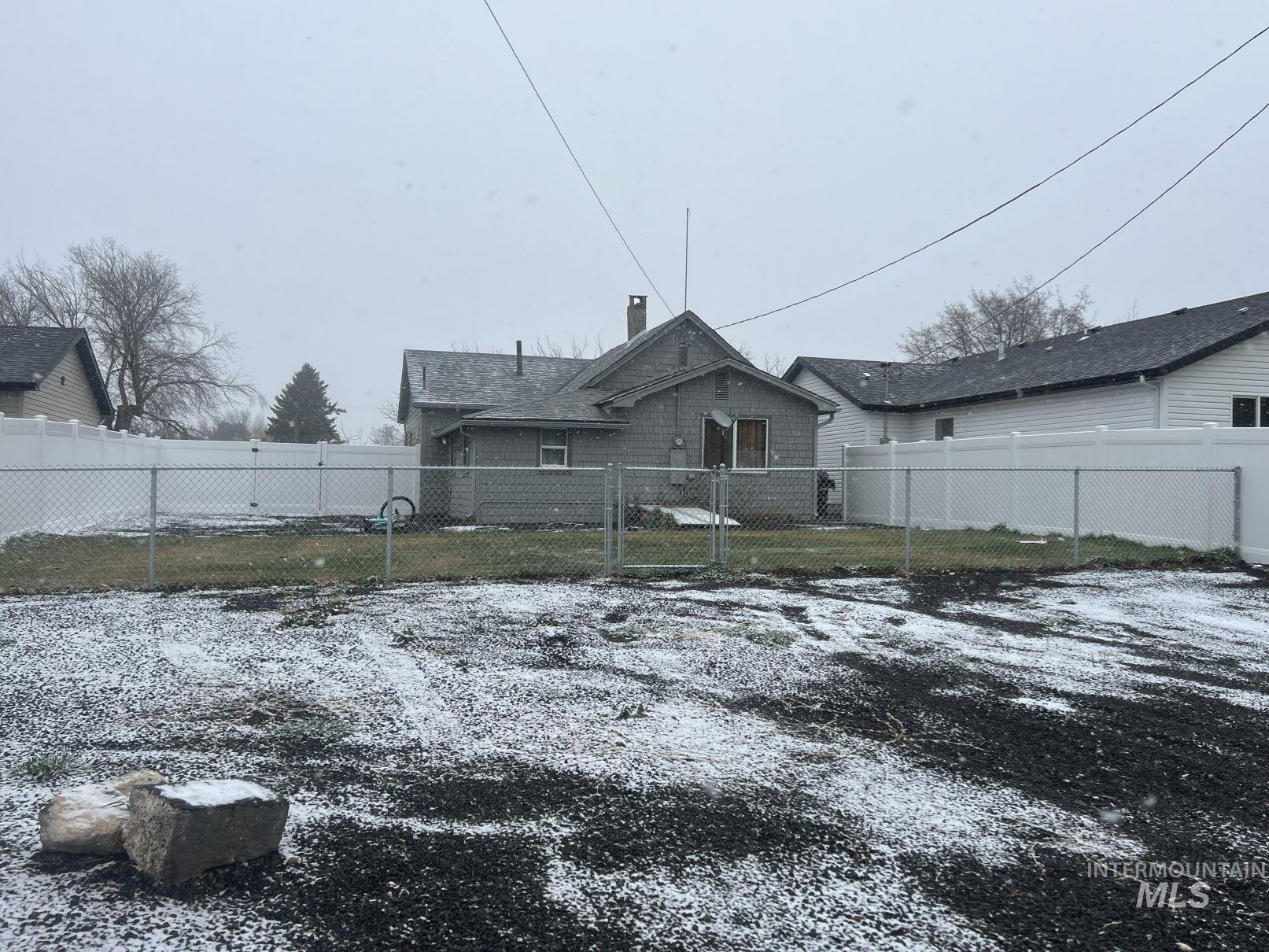 Snow covered rear of property featuring a chimney and a gate