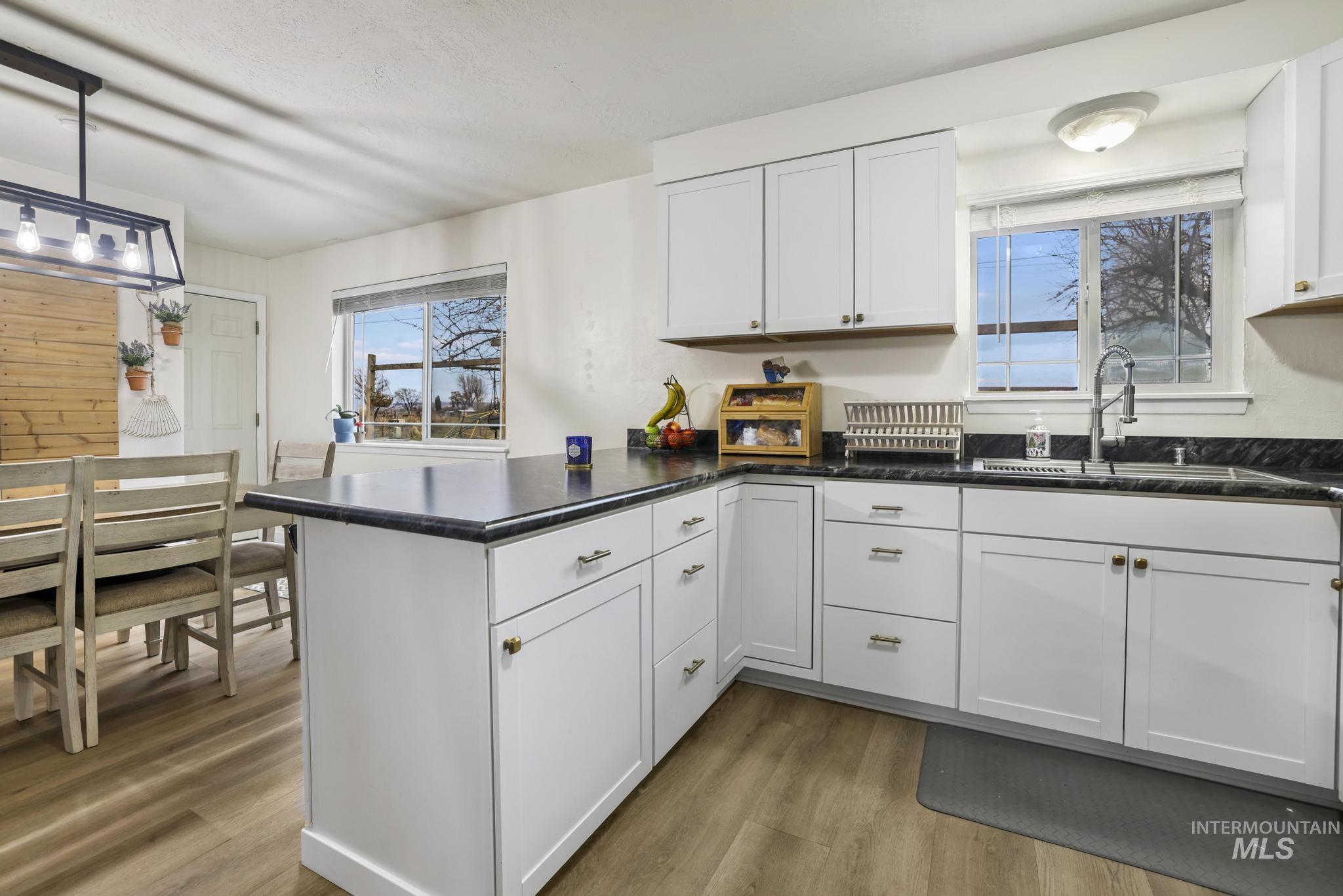 Kitchen featuring a peninsula, white cabinets, light wood-style floors, and hanging light fixtures