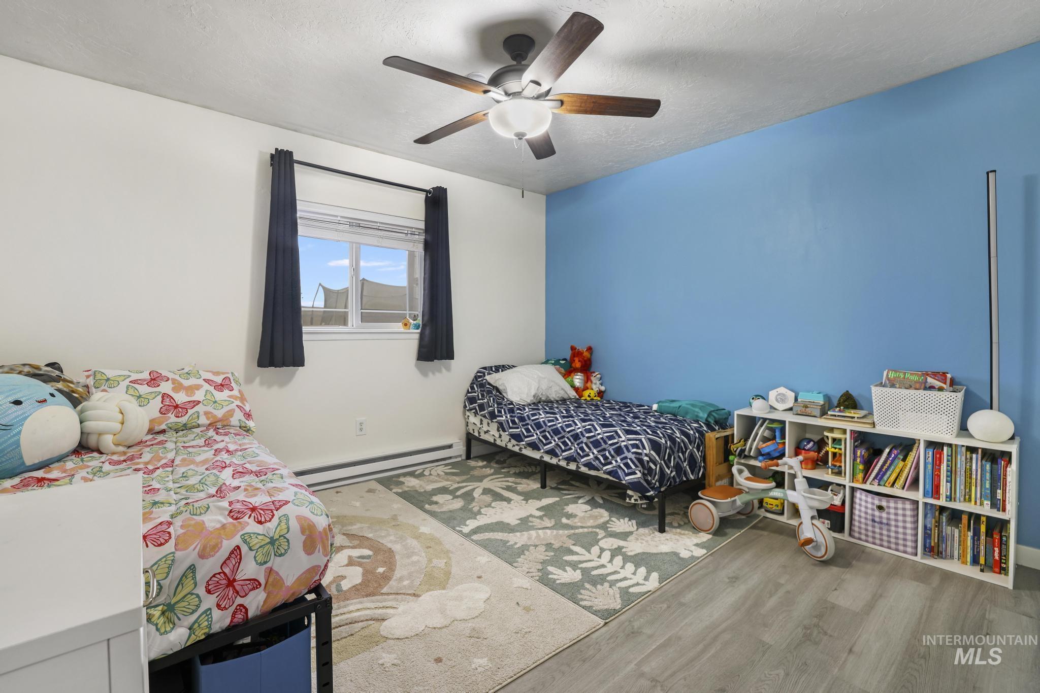 Bedroom featuring baseboard heating, light wood finished floors, a ceiling fan, and a textured ceiling