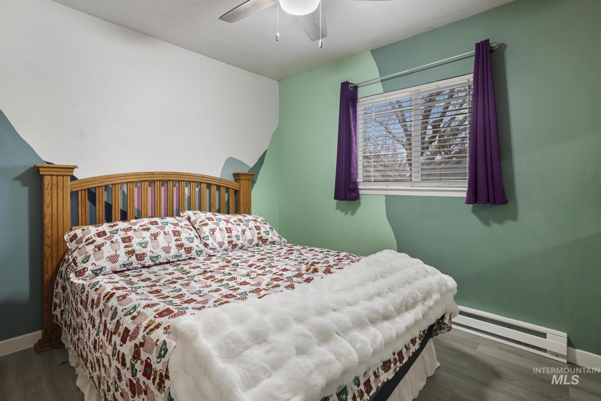 Bedroom featuring baseboard heating, dark wood-style floors, and a ceiling fan
