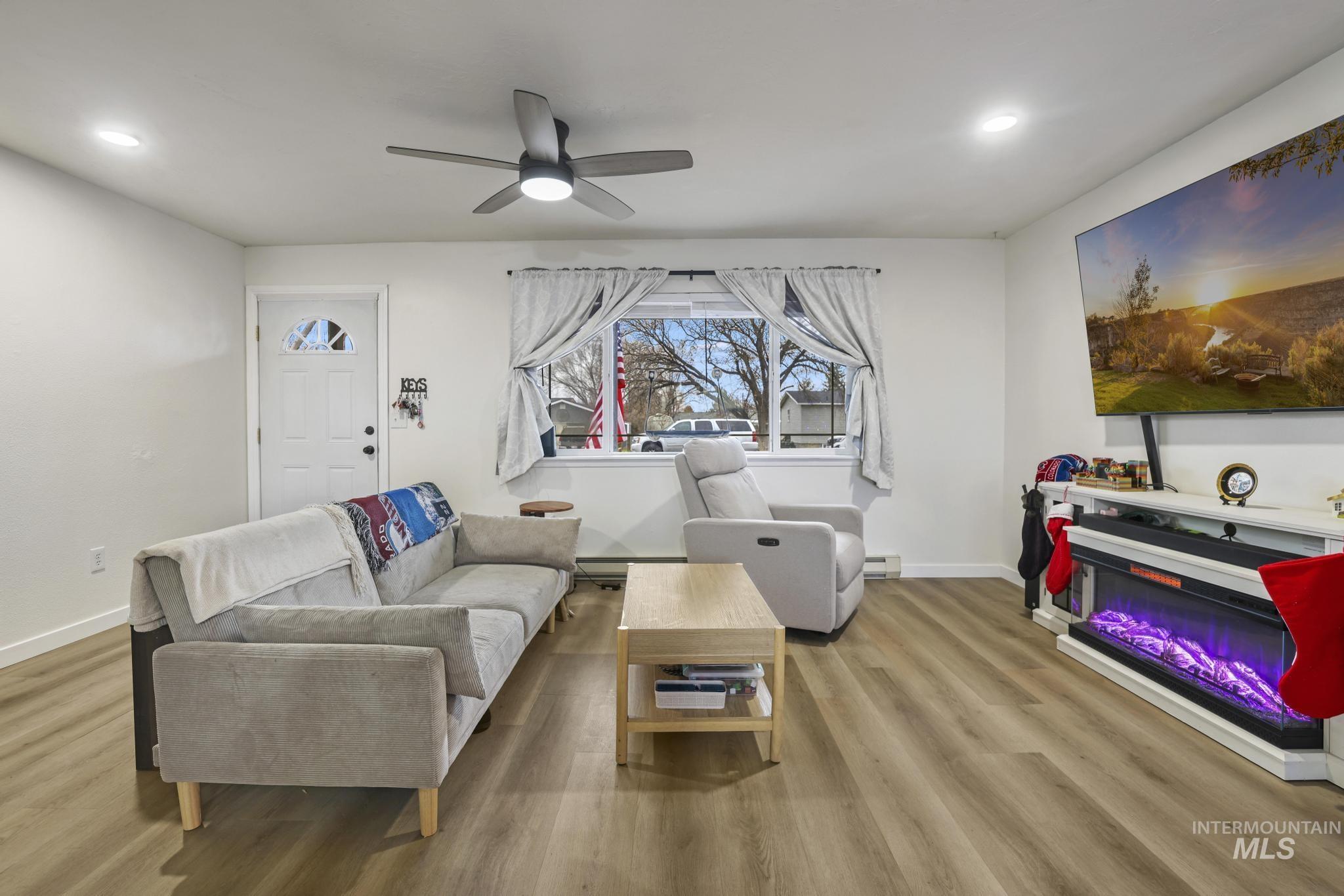 Living room with ceiling fan, wood finished floors, recessed lighting, a glass covered fireplace, and a baseboard radiator