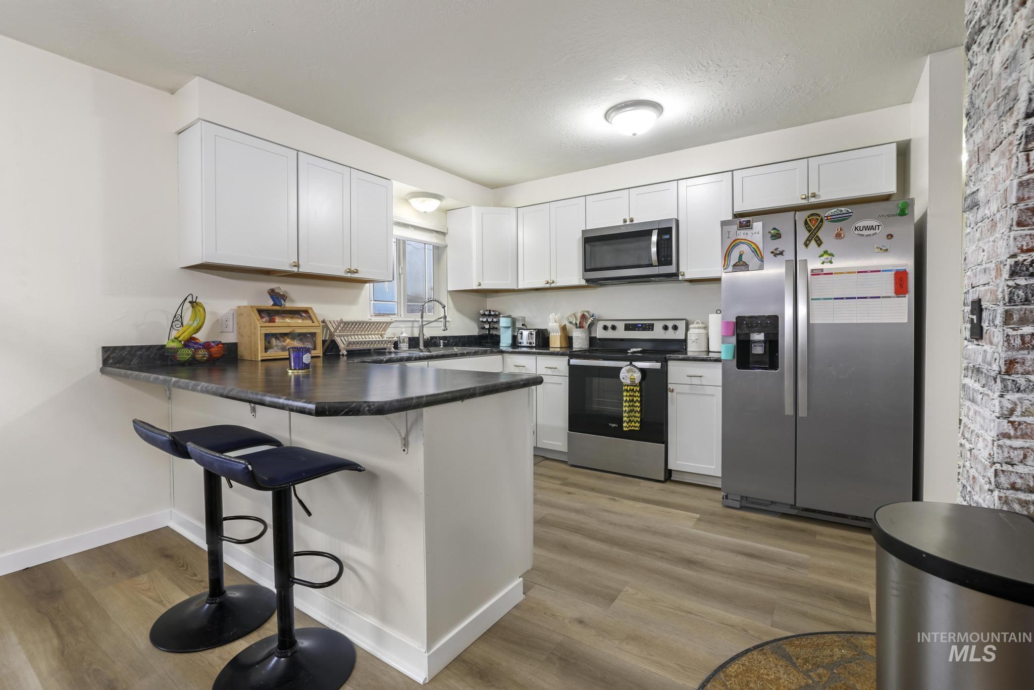 Kitchen featuring a kitchen breakfast bar, stainless steel appliances, dark countertops, a peninsula, and light wood-style floors