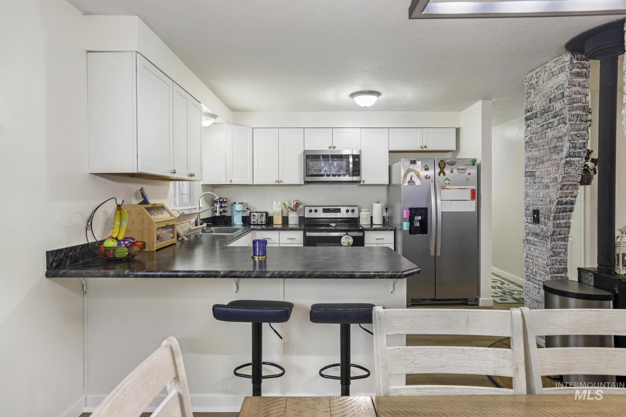 Kitchen with stainless steel appliances, dark countertops, white cabinets, and a kitchen bar