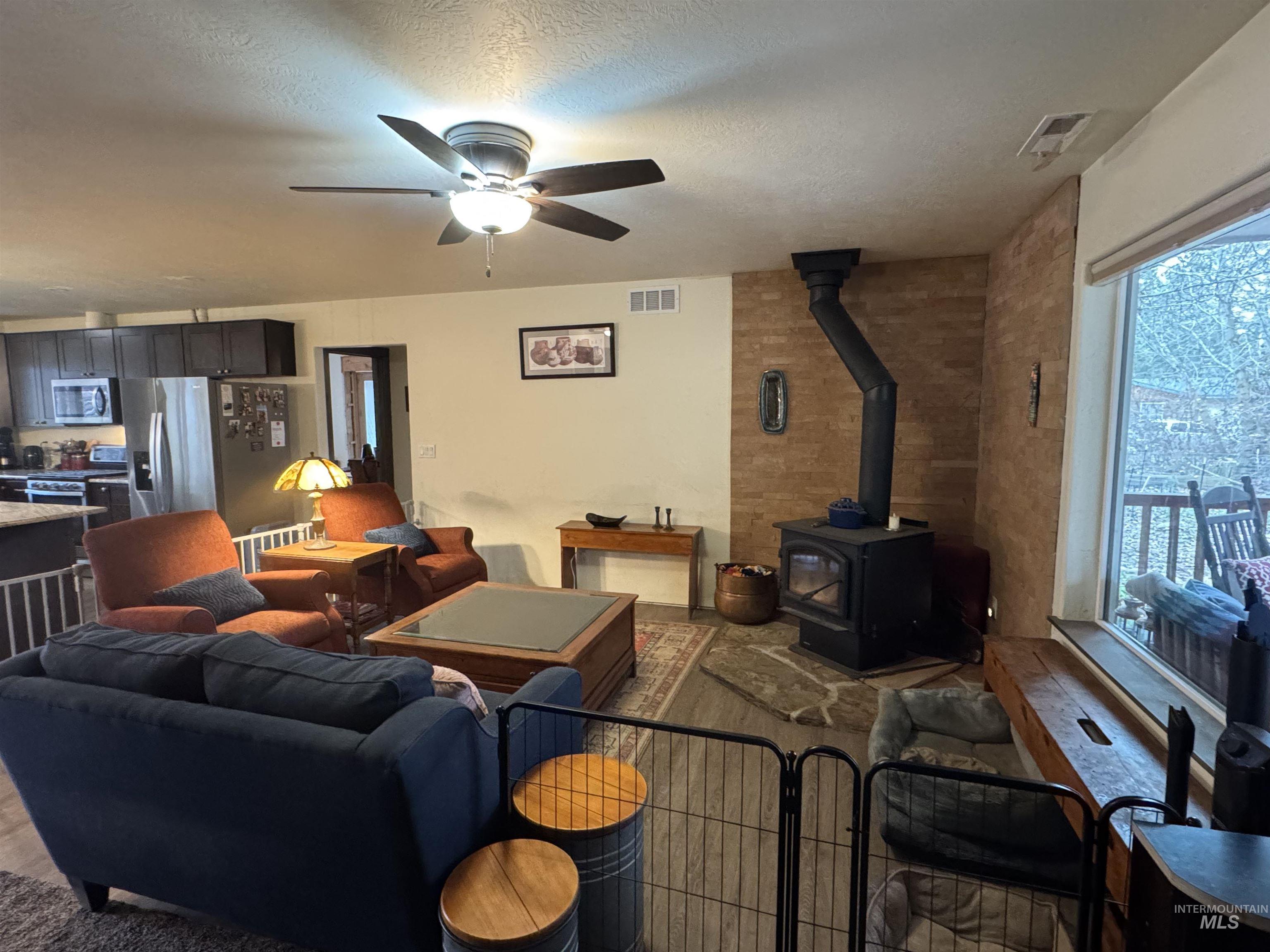 Living area with a wood stove, a textured ceiling, and a ceiling fan