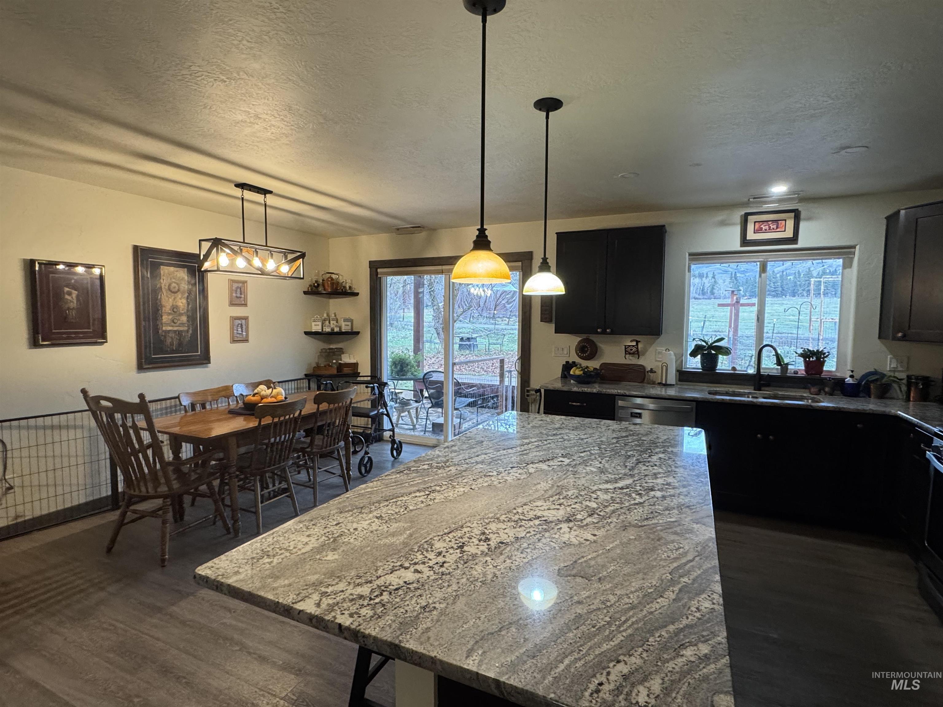 Kitchen featuring dark stone countertops, pendant lighting, a center island, a textured ceiling, and dark cabinetry