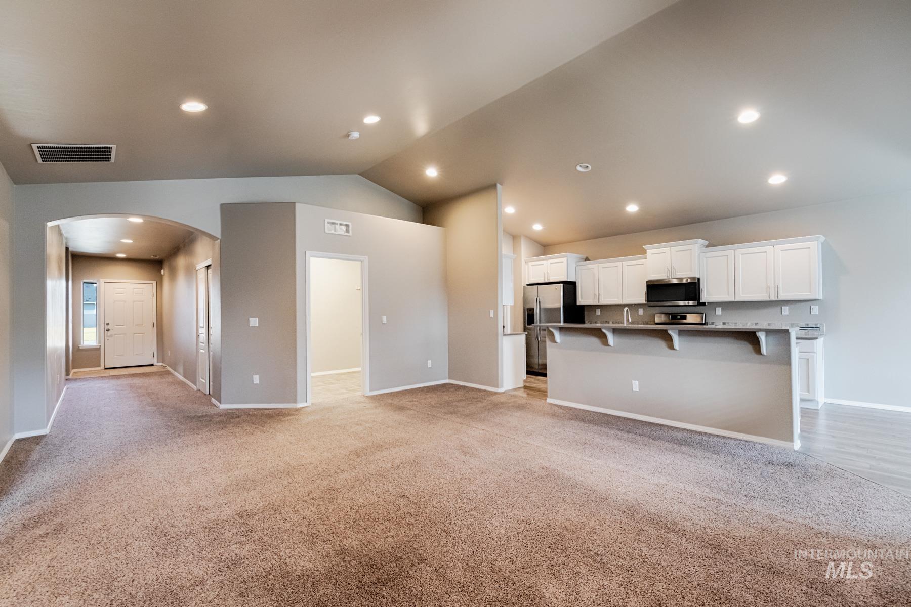 Kitchen featuring open floor plan, arched walkways, white cabinetry, light colored carpet, and recessed lighting