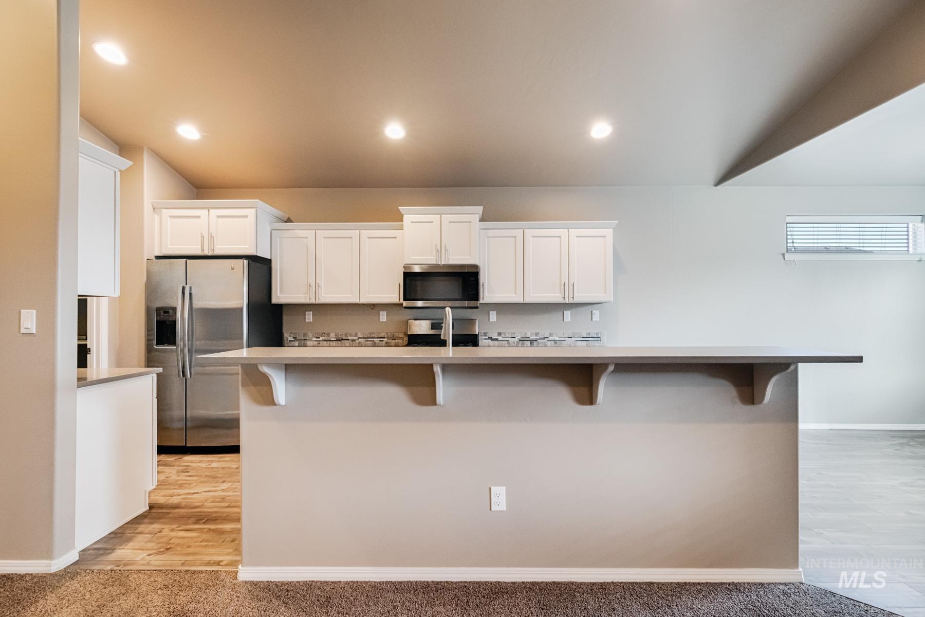 Kitchen featuring stainless steel appliances, white cabinetry, a breakfast bar, light countertops, and recessed lighting