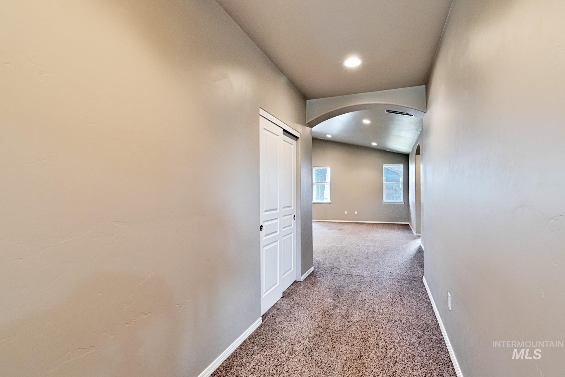 Hall with arched walkways, vaulted ceiling, carpet flooring, and recessed lighting