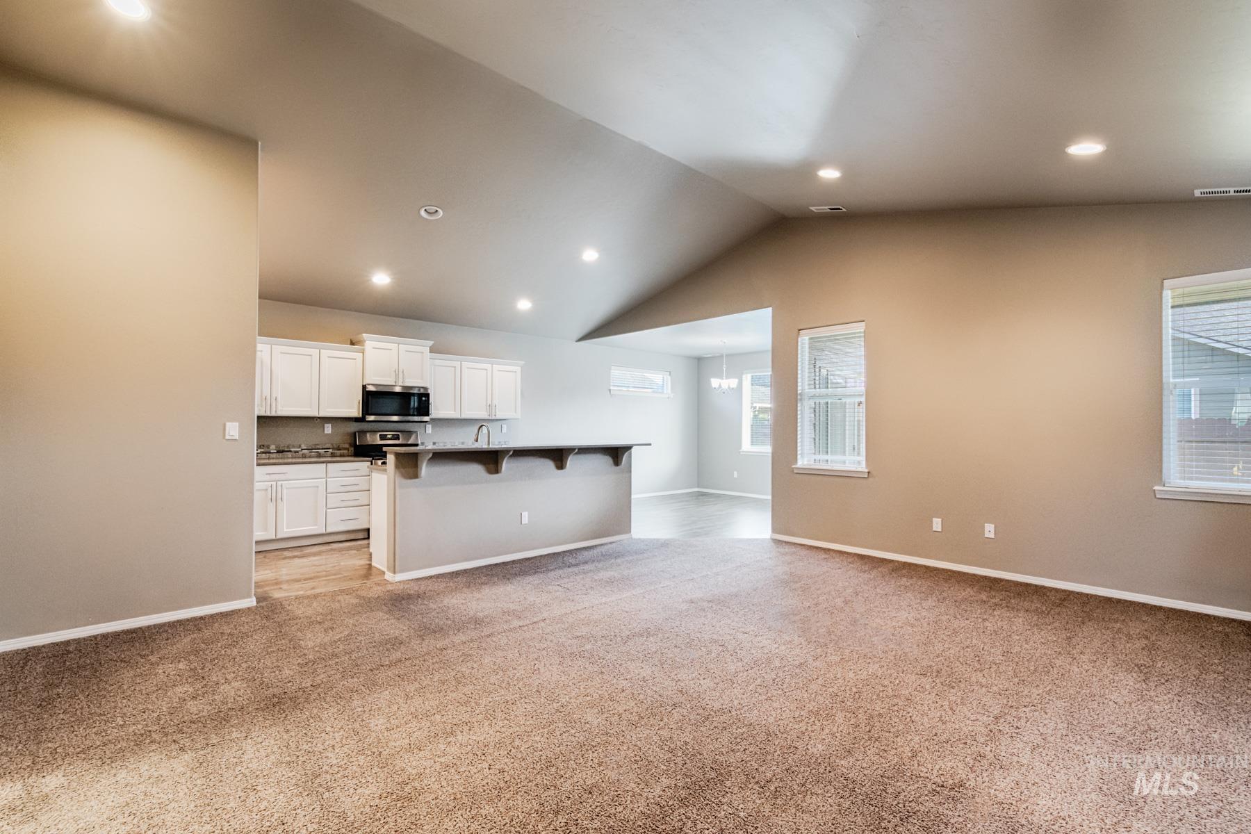 Kitchen with a breakfast bar area, white cabinetry, vaulted ceiling, open floor plan, and recessed lighting