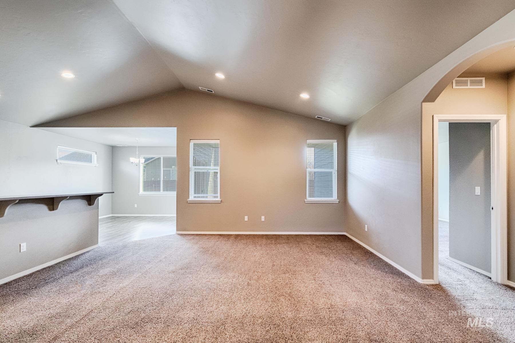 Empty room with light colored carpet, lofted ceiling, a chandelier, and recessed lighting