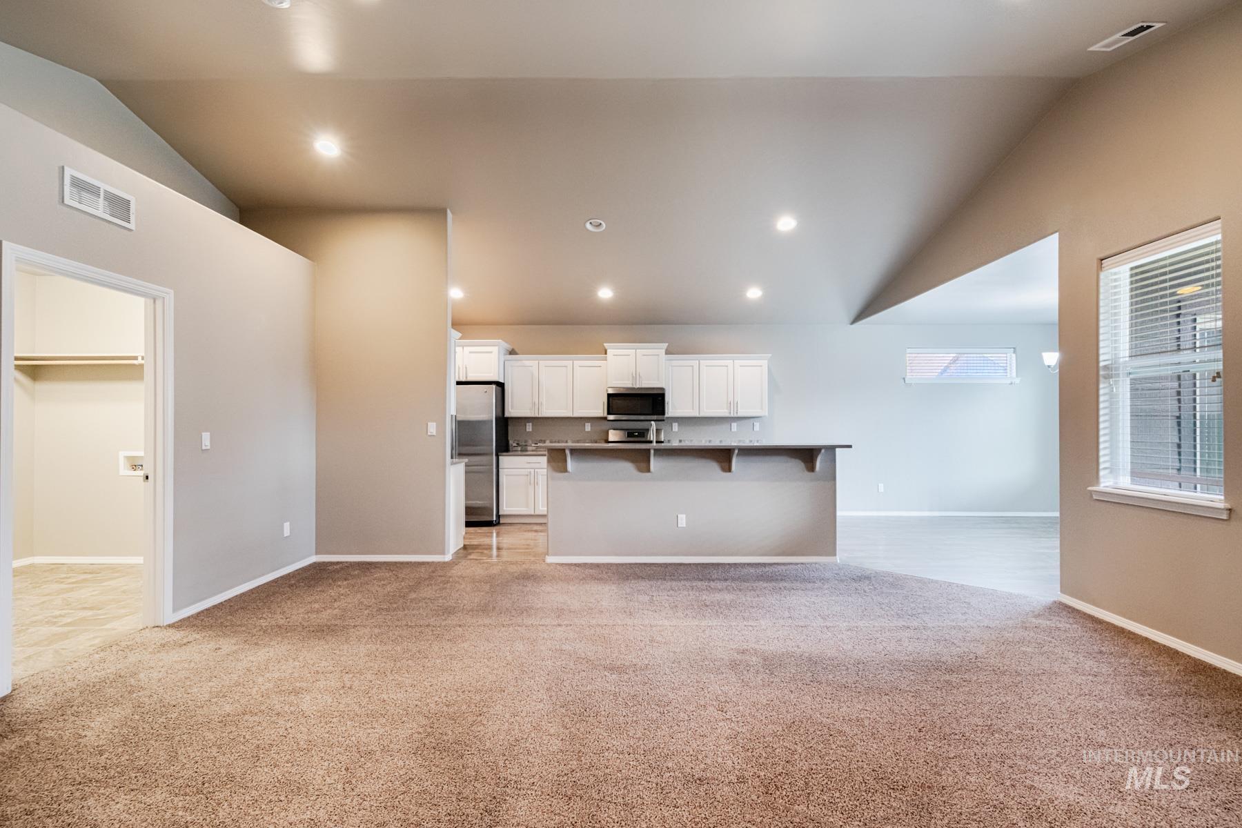 Kitchen featuring lofted ceiling, open floor plan, white cabinetry, light colored carpet, and a breakfast bar
