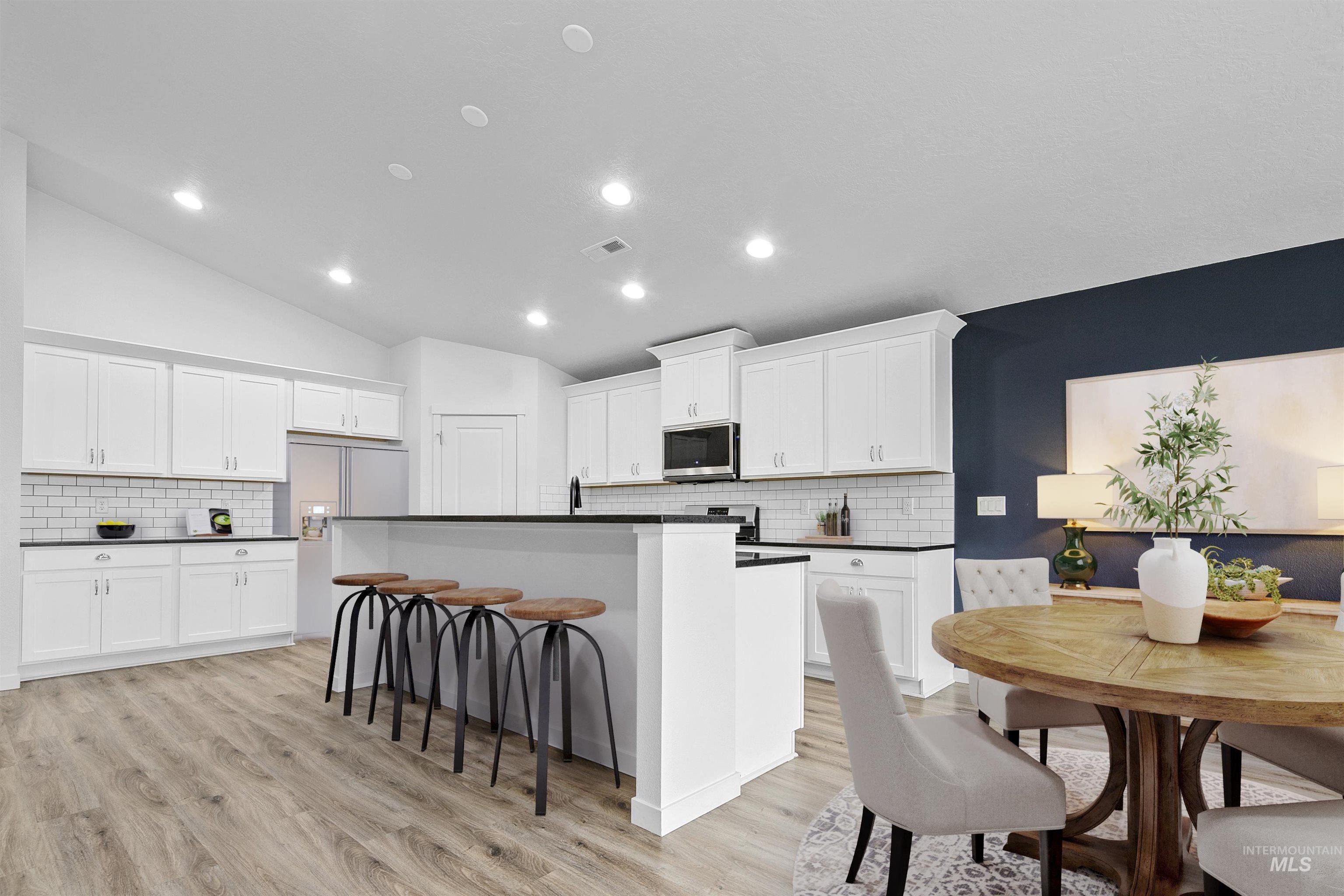 Kitchen featuring dark countertops, a center island with sink, vaulted ceiling, backsplash, and recessed lighting