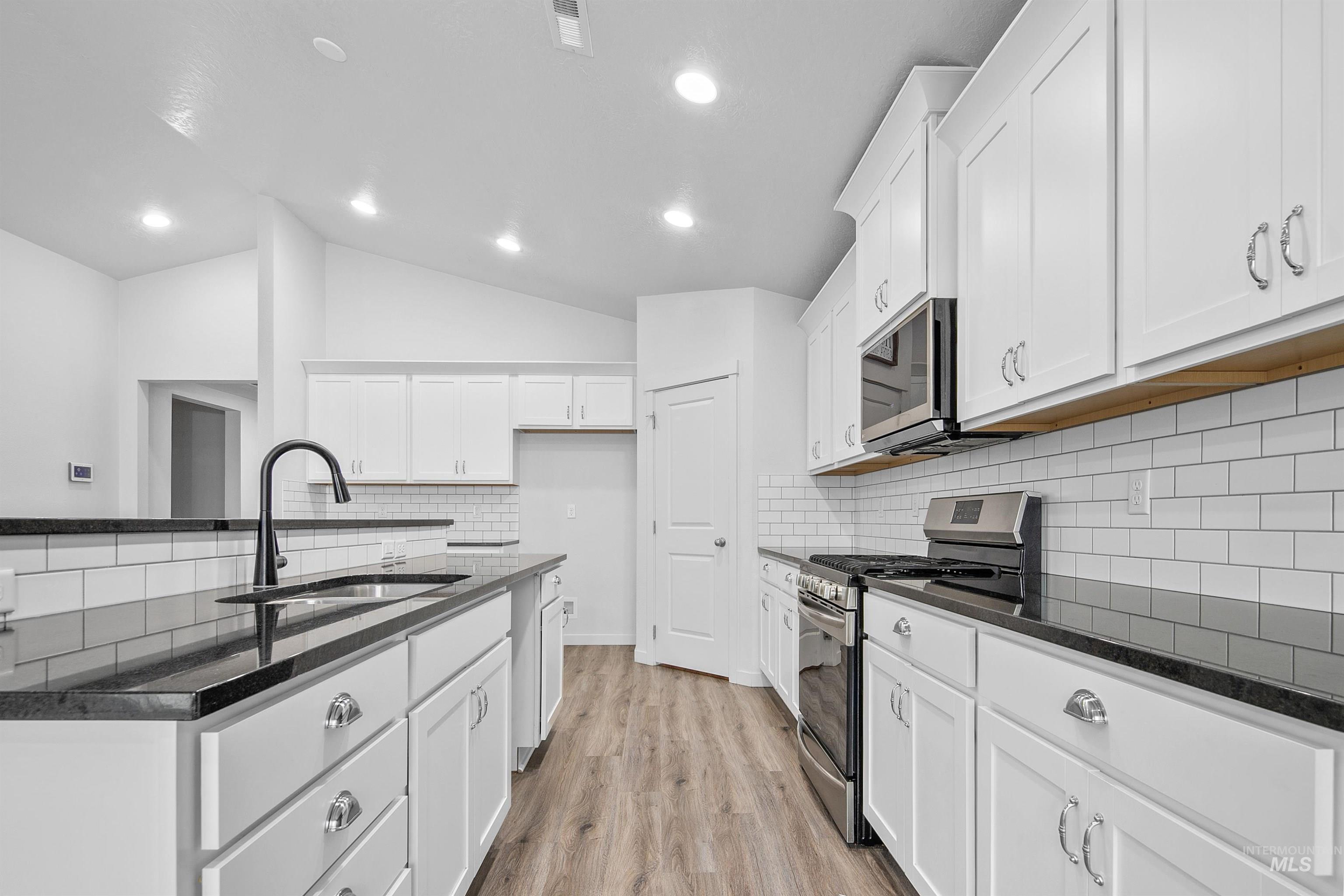 Kitchen featuring appliances with stainless steel finishes, dark stone counters, decorative backsplash, white cabinetry, and vaulted ceiling