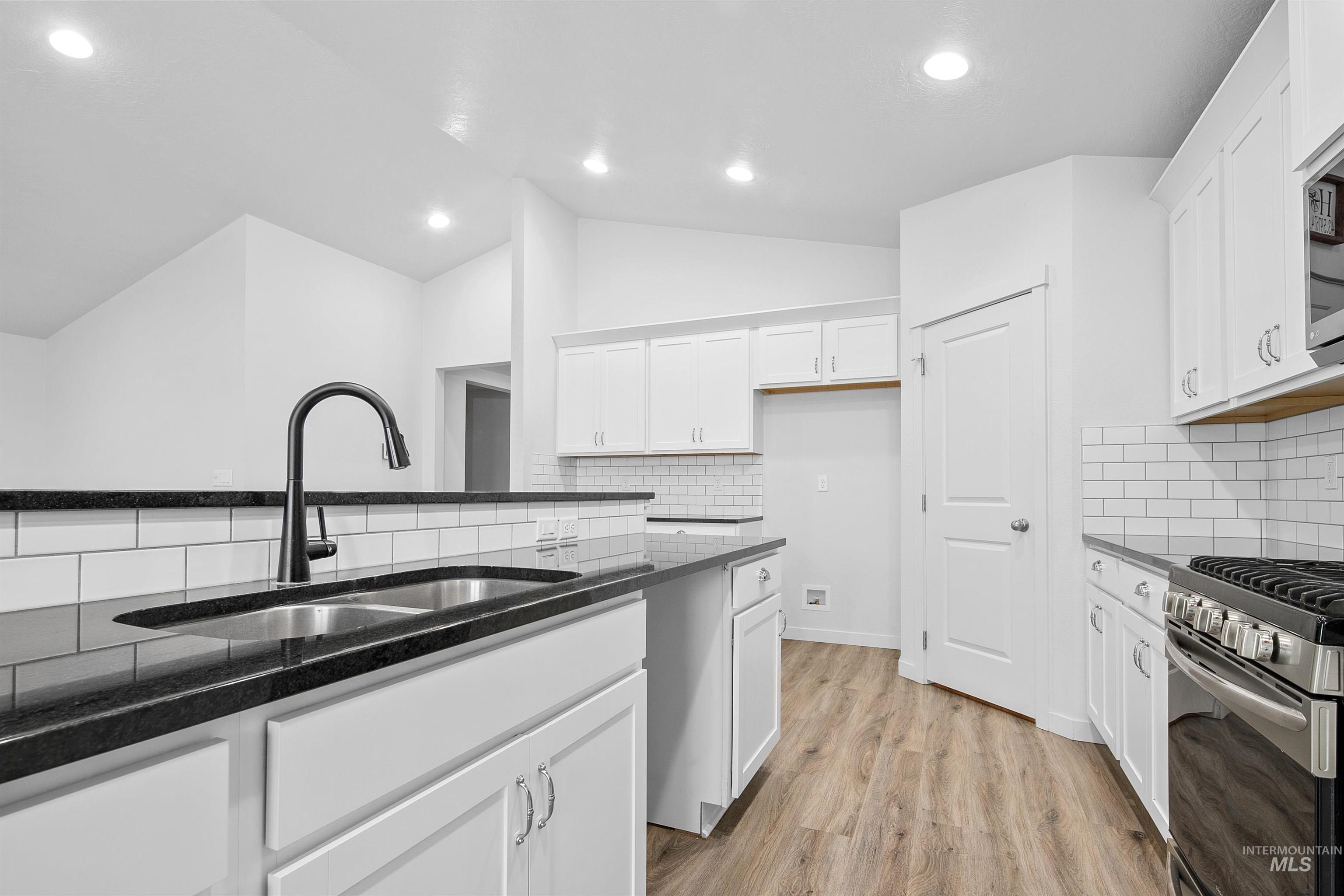 Kitchen with white cabinets, dark stone counters, vaulted ceiling, light wood-style flooring, and stainless steel appliances