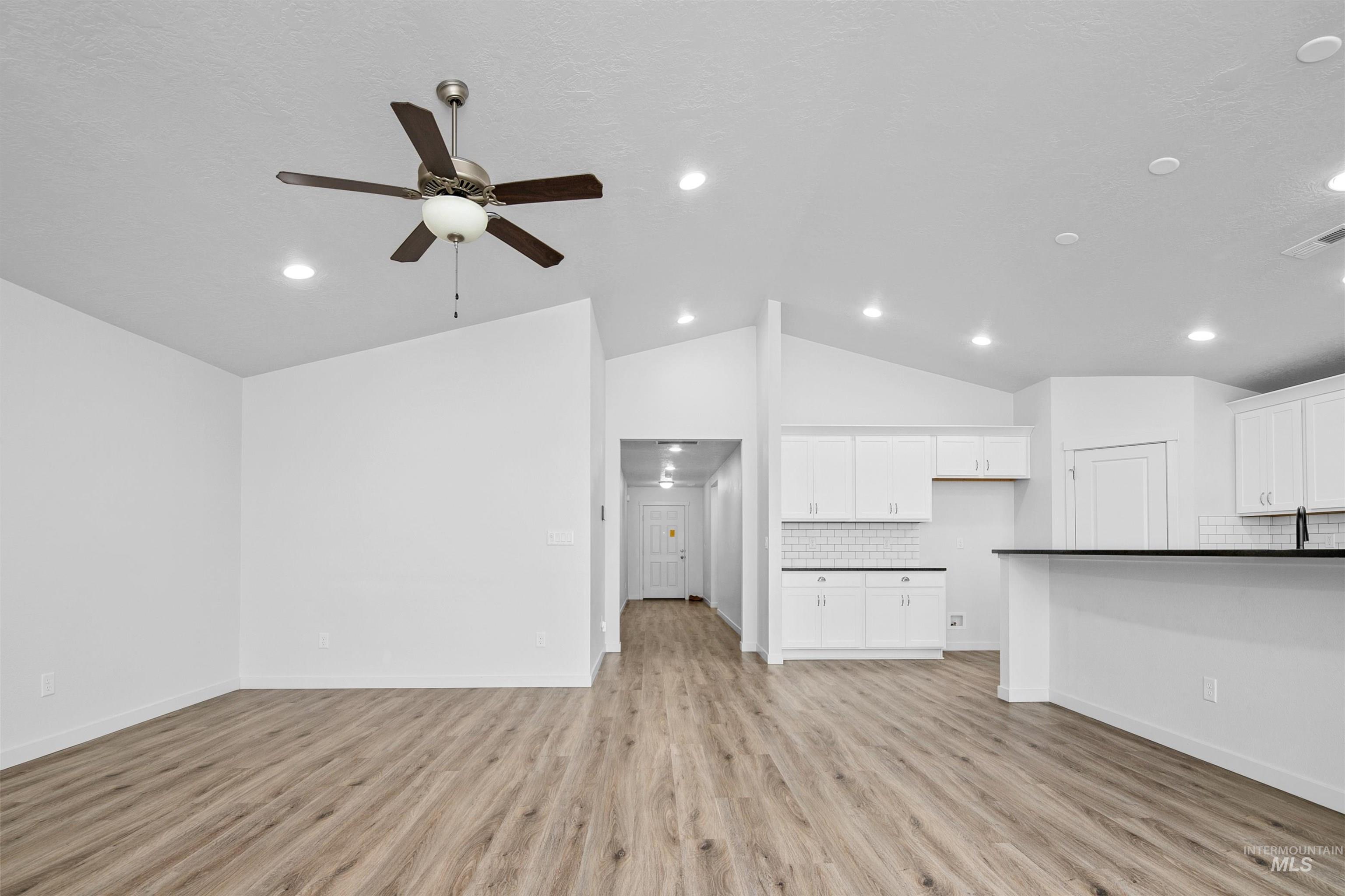 Unfurnished living room featuring vaulted ceiling, light wood finished floors, and ceiling fan