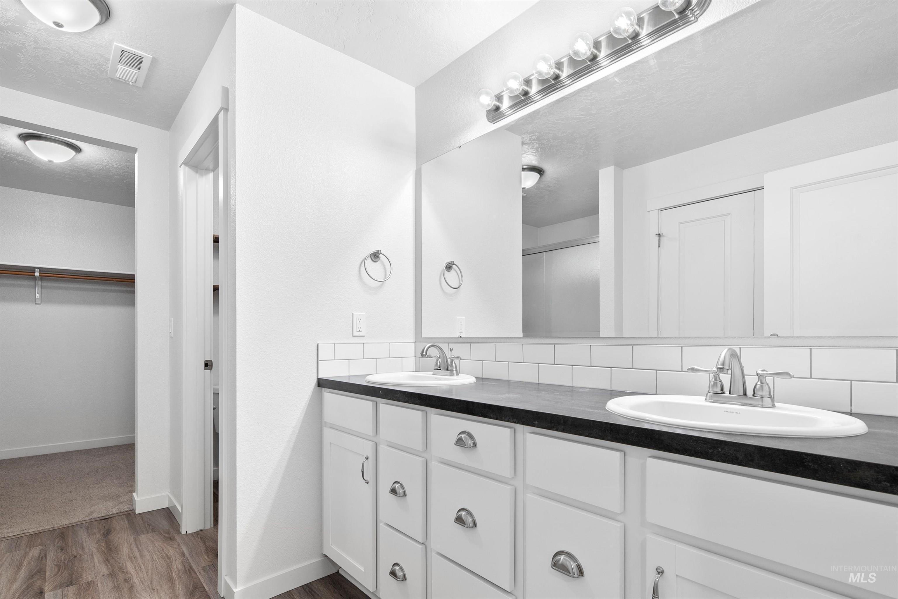 Full bathroom featuring a walk in closet, double vanity, decorative backsplash, a stall shower, and dark wood finished floors