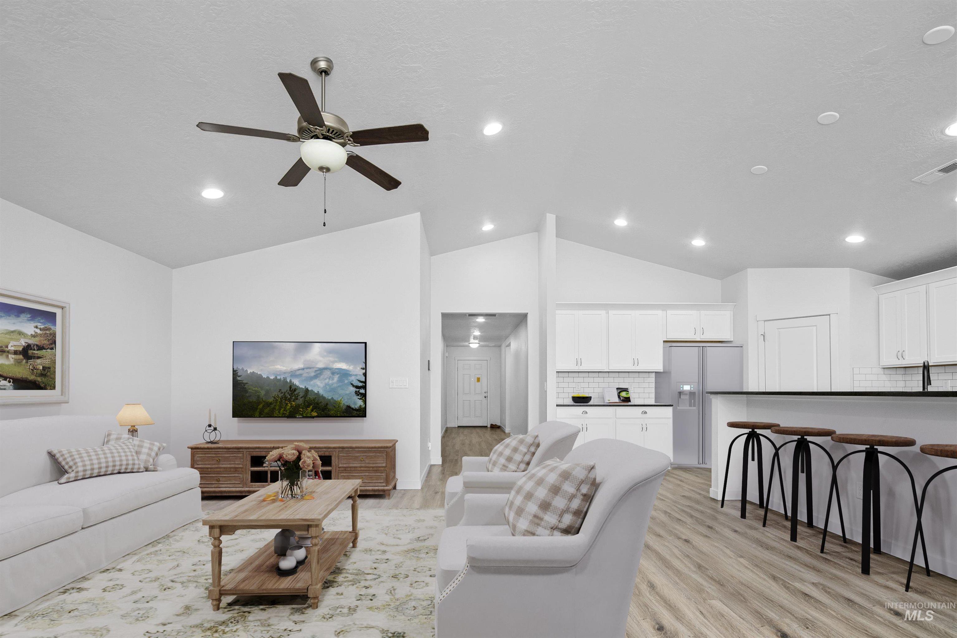 Living area featuring vaulted ceiling, light wood-style flooring, and a ceiling fan