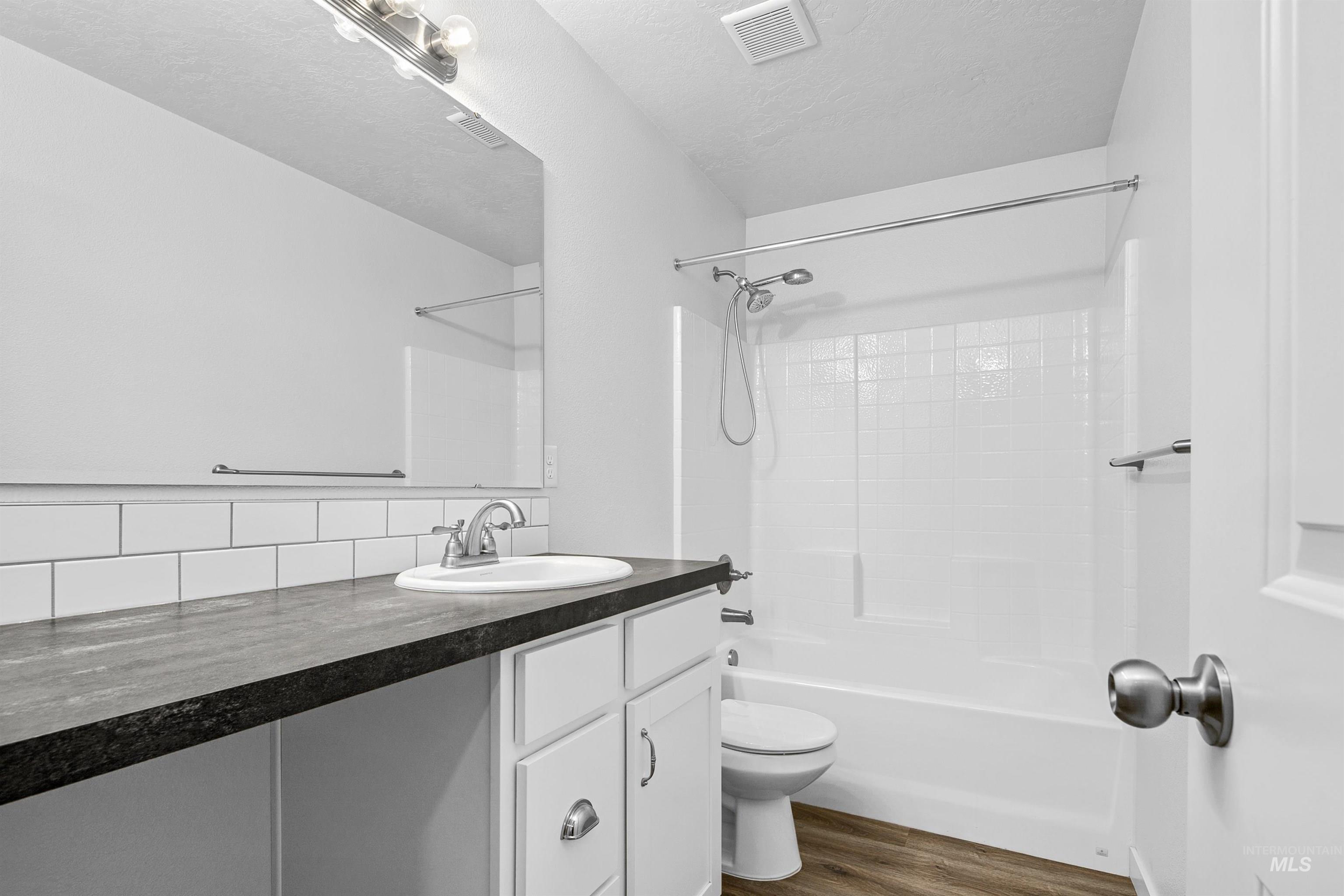 Bathroom featuring vanity, bathing tub / shower combination, dark wood-style floors, a textured ceiling, and tasteful backsplash