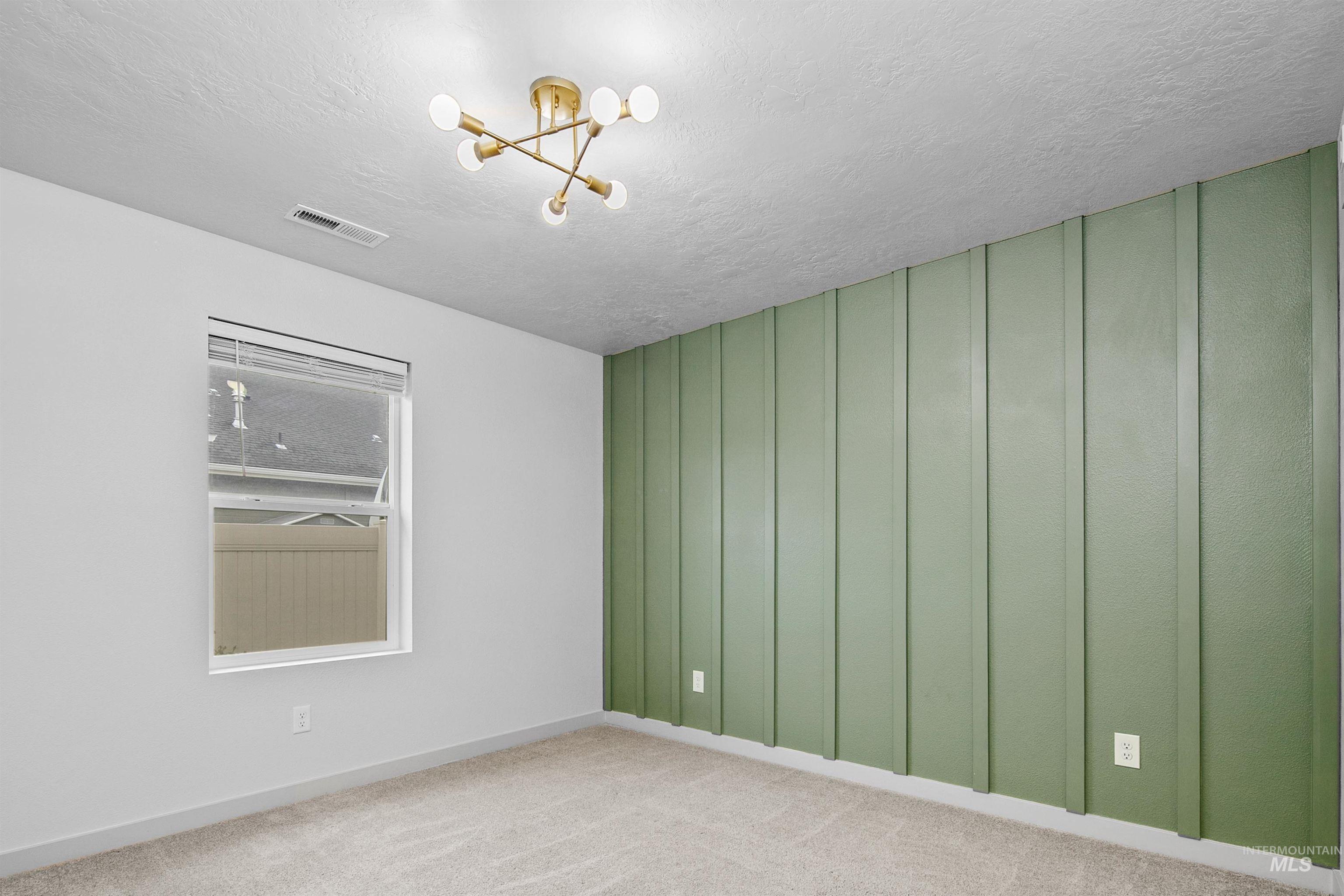 Carpeted spare room featuring a chandelier, a textured ceiling, and a decorative wall