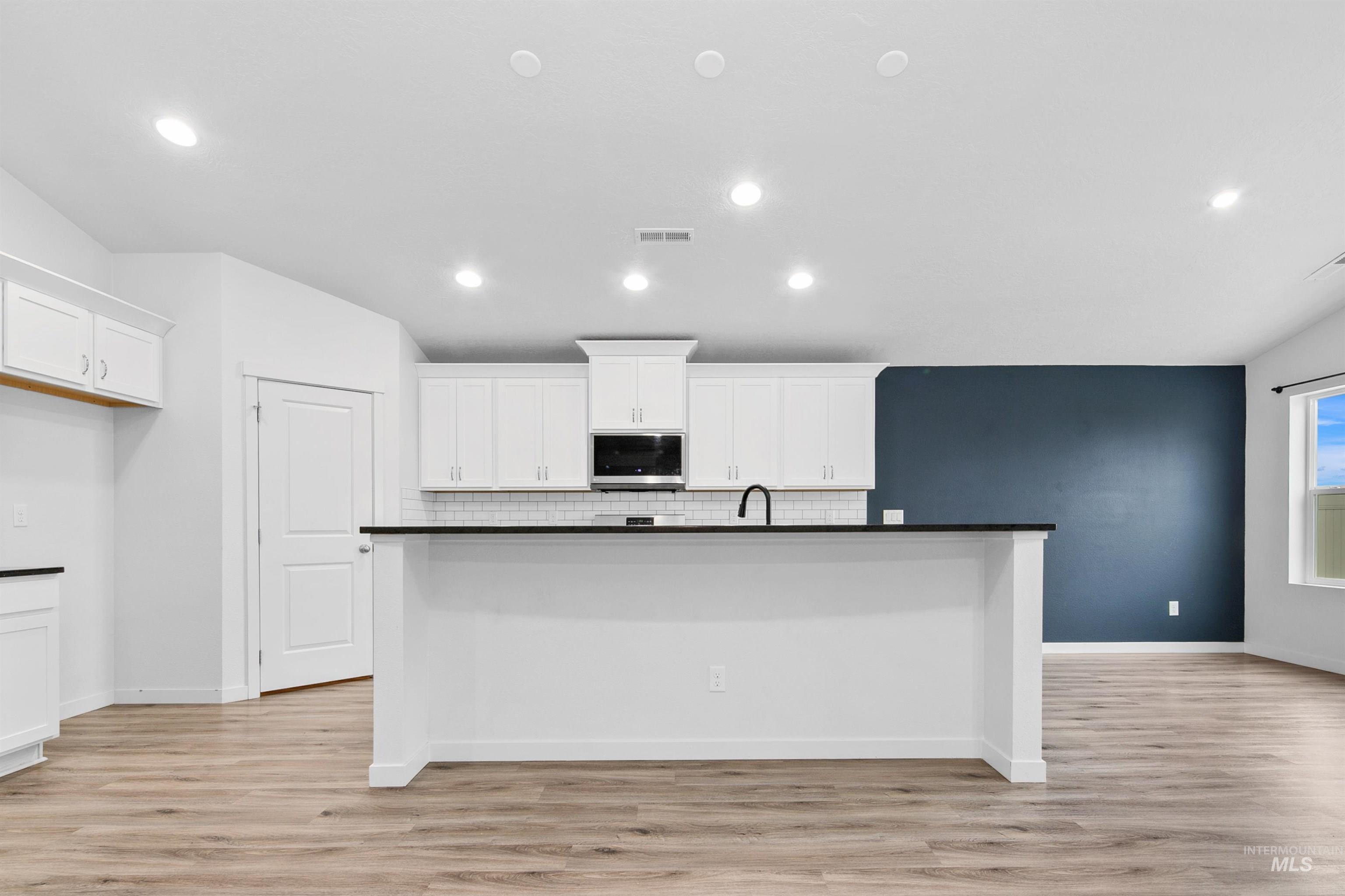 Kitchen featuring white cabinetry, a center island with sink, light wood-type flooring, stainless steel microwave, and recessed lighting