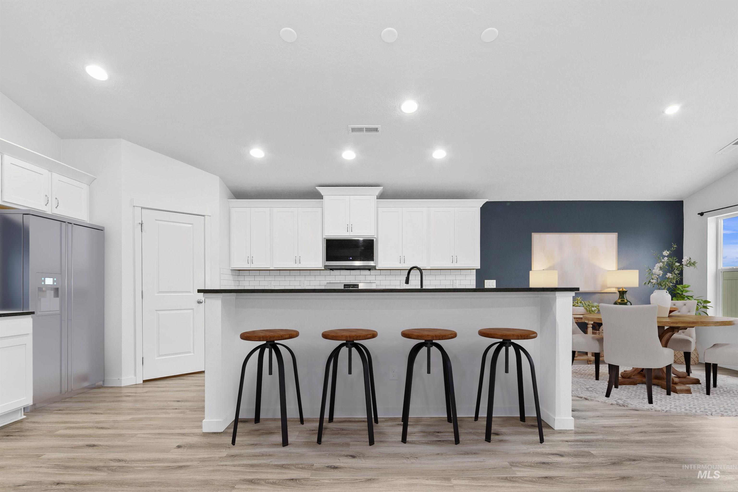 Kitchen featuring dark countertops, high quality fridge, white cabinetry, an island with sink, and decorative backsplash