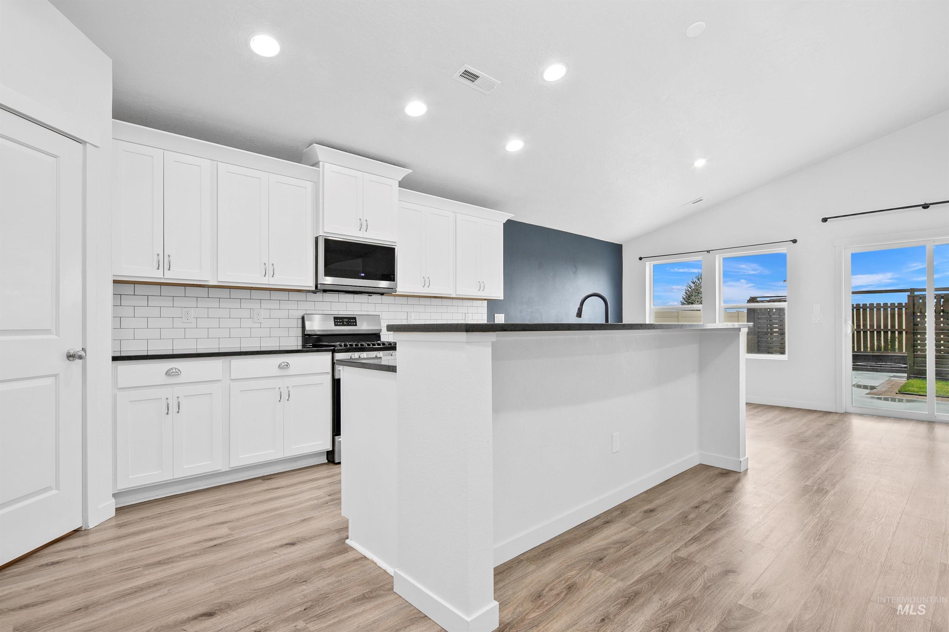 Kitchen with recessed lighting, a kitchen island with sink, lofted ceiling, stainless steel appliances, and white cabinets