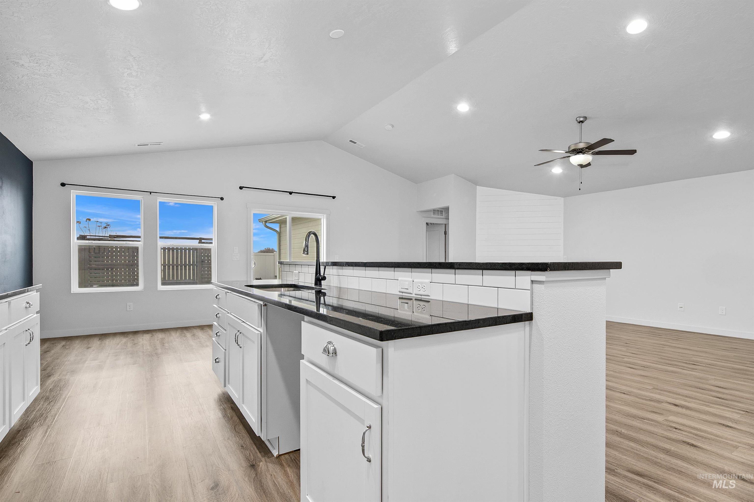 Kitchen featuring white cabinets, light wood-style floors, open floor plan, a center island with sink, and a ceiling fan