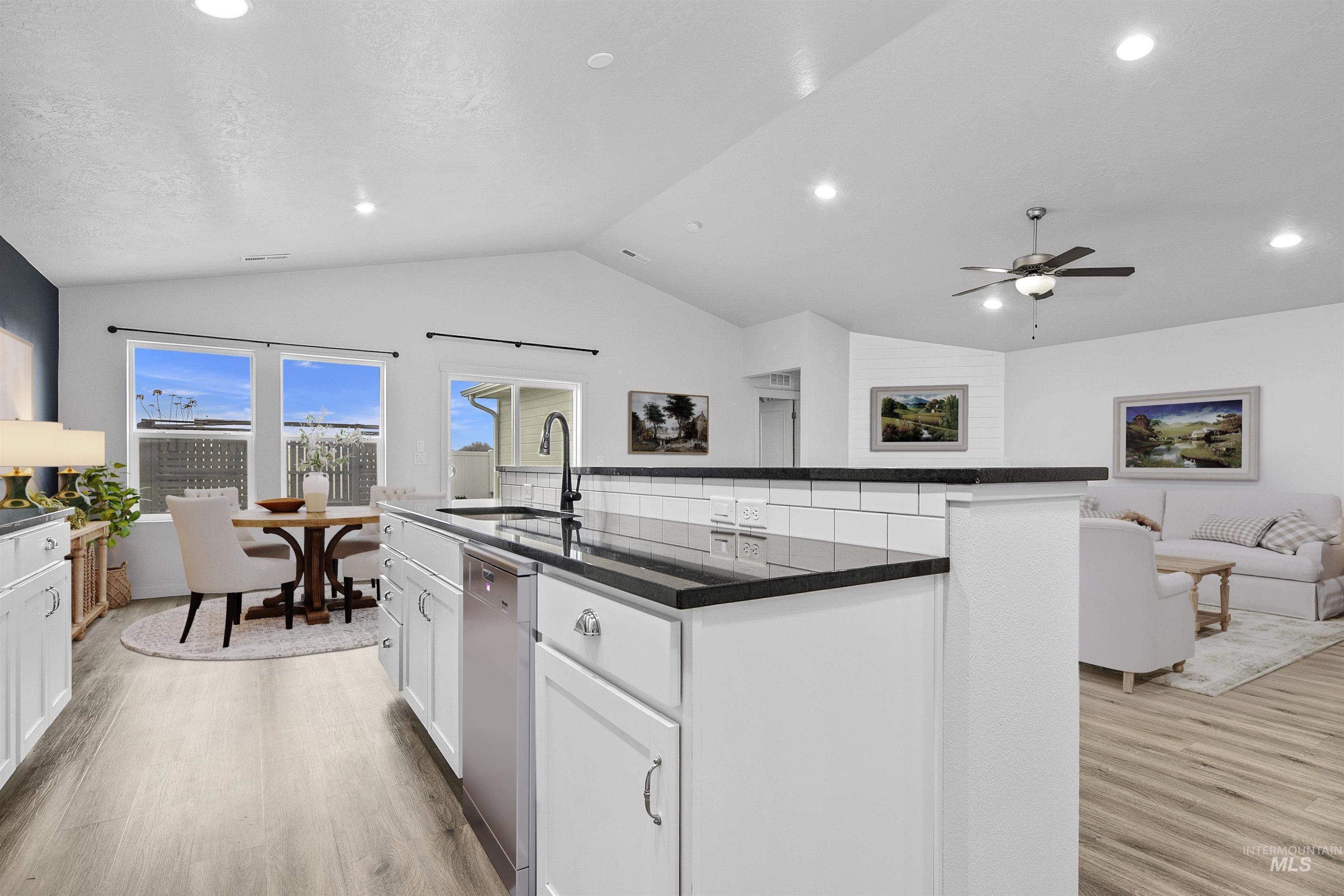Kitchen with white cabinets, open floor plan, a center island with sink, vaulted ceiling, and light wood finished floors
