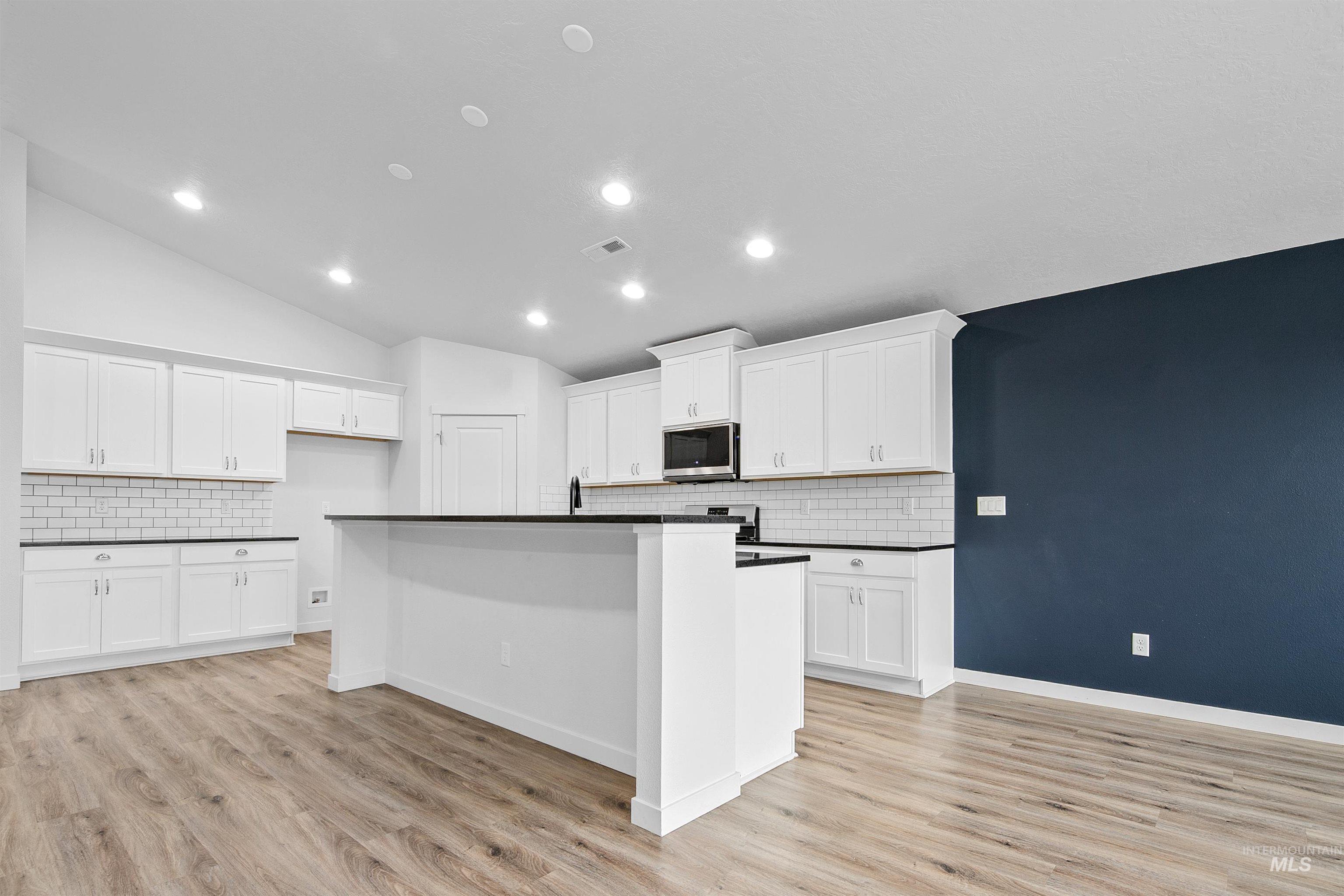 Kitchen featuring recessed lighting, white cabinetry, an island with sink, backsplash, and lofted ceiling