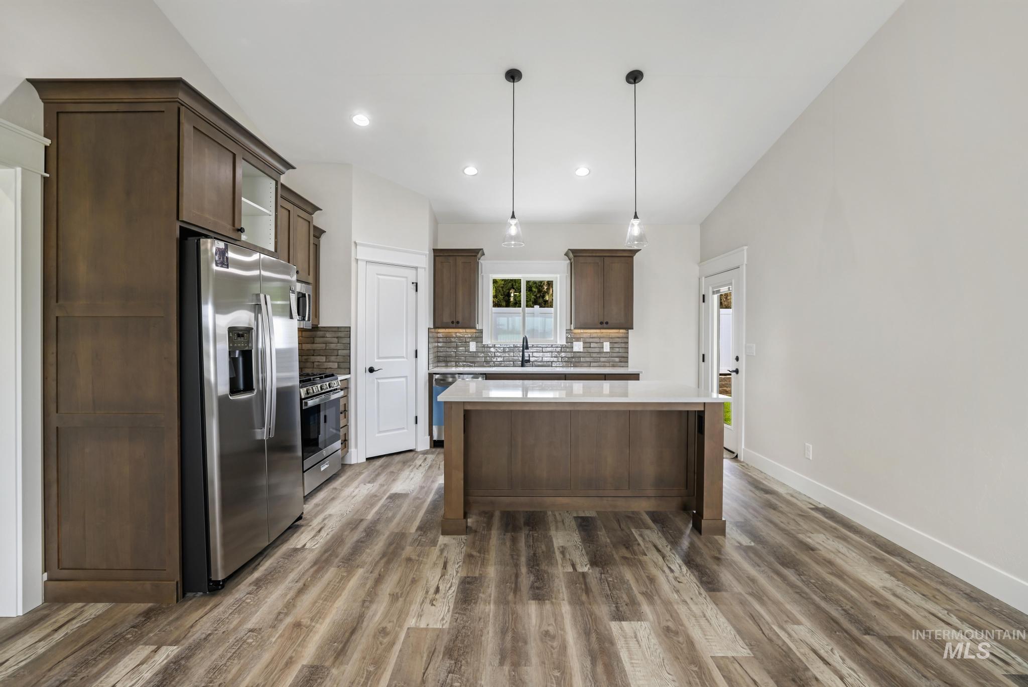 Kitchen with appliances with stainless steel finishes, dark brown cabinets, decorative light fixtures, dark wood-style flooring, and recessed lighting