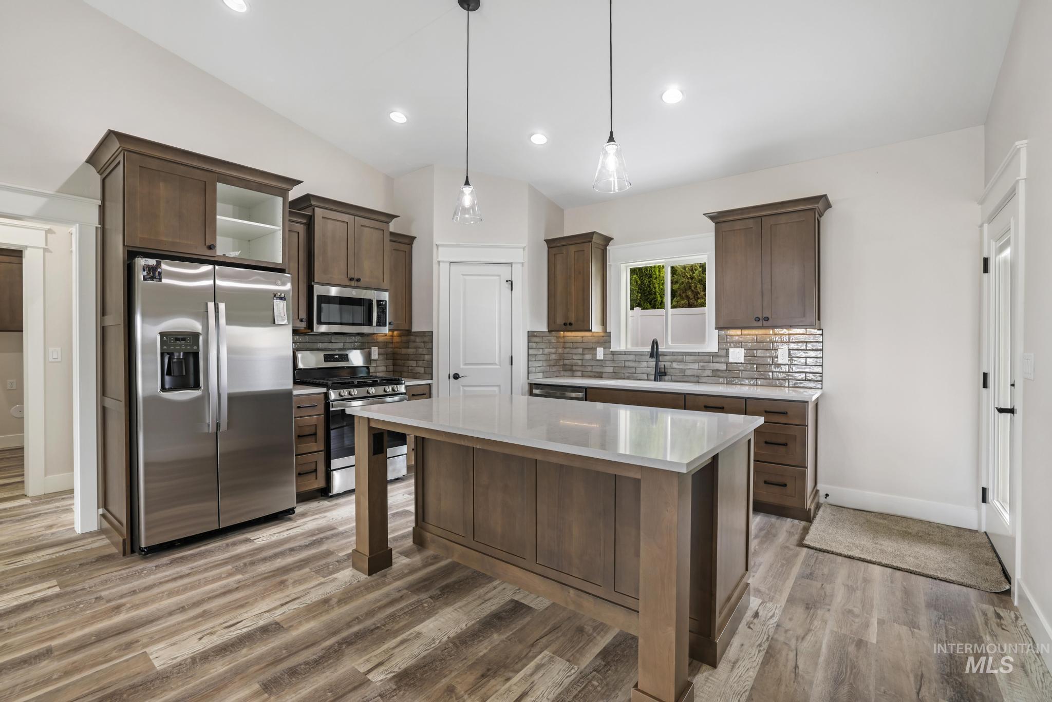 Kitchen featuring appliances with stainless steel finishes, dark brown cabinetry, pendant lighting, a center island, and light wood-style flooring
