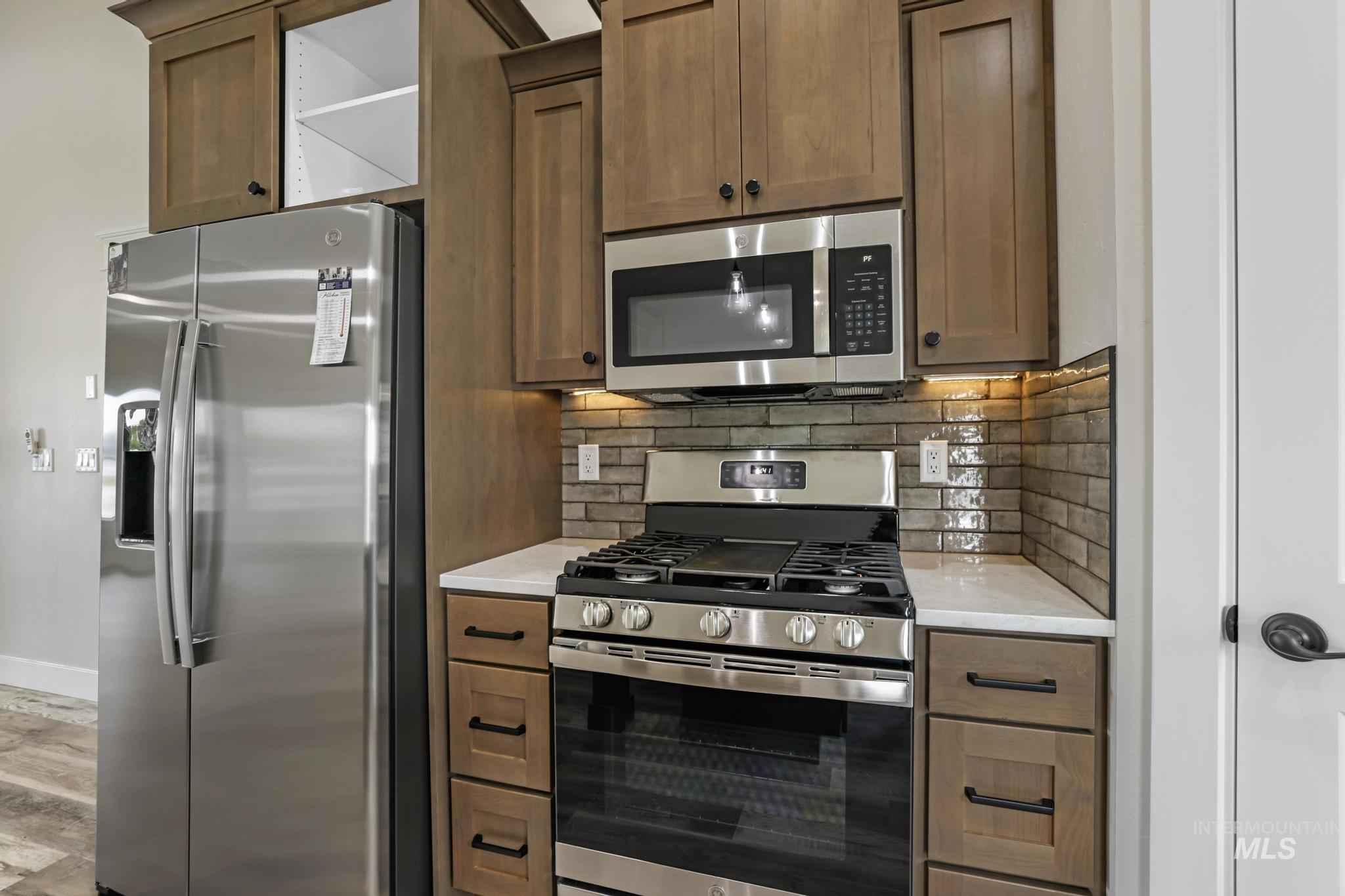 Kitchen featuring appliances with stainless steel finishes, tasteful backsplash, brown cabinetry, and light stone countertops