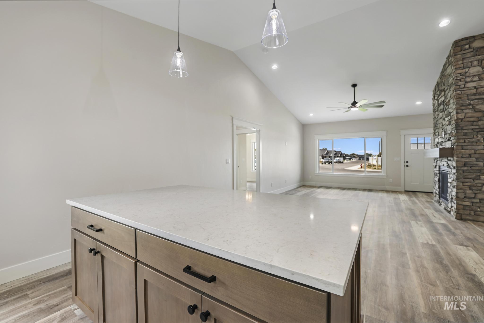 Kitchen with a kitchen island, hanging light fixtures, light wood-type flooring, a stone fireplace, and open floor plan