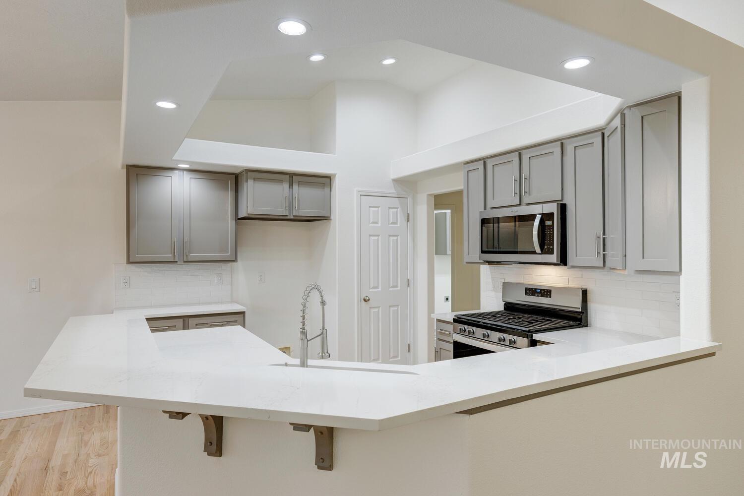 Kitchen with a peninsula, tasteful backsplash, stainless steel appliances, recessed lighting, and gray cabinets