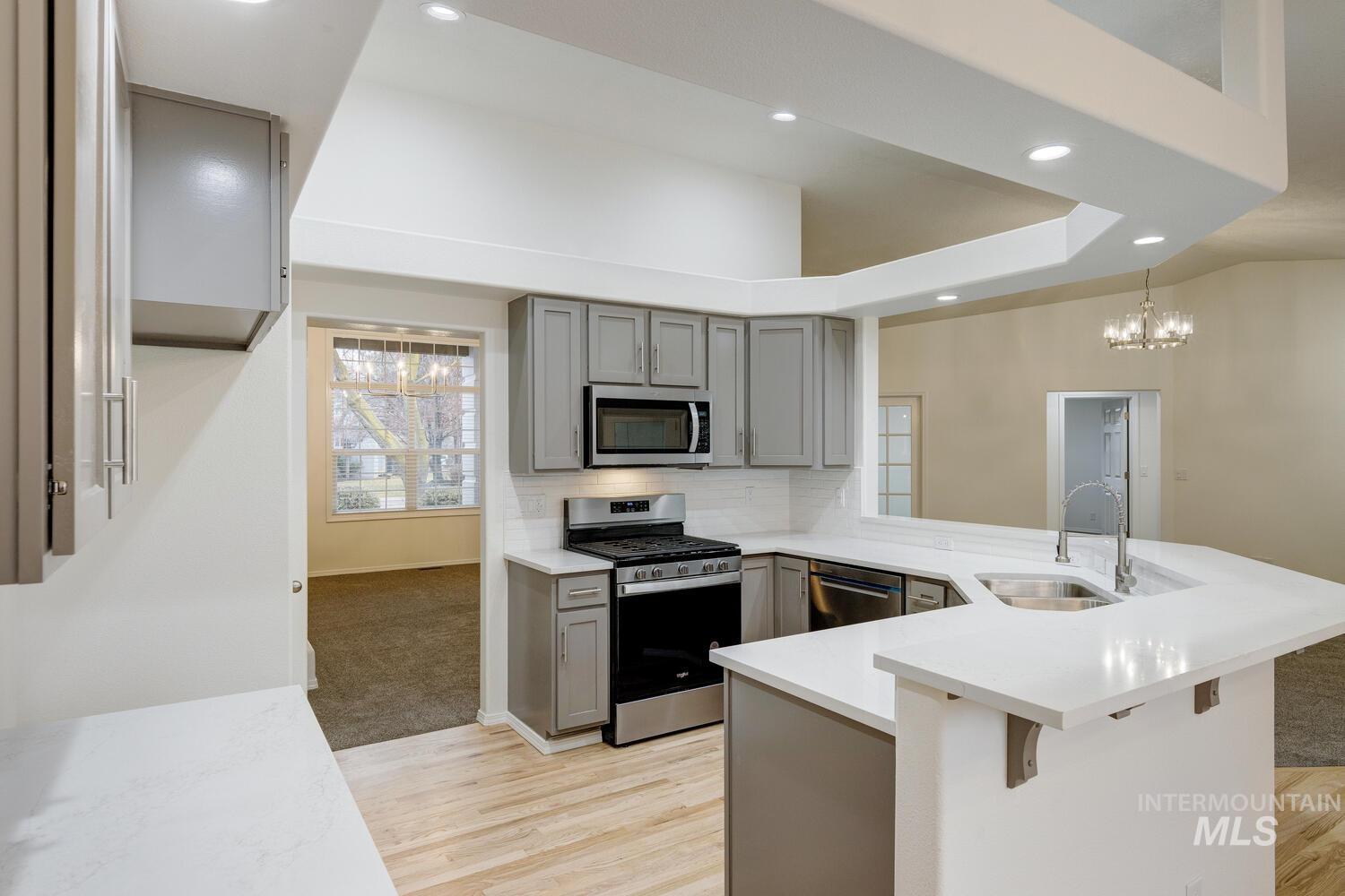 Kitchen with gray cabinetry, stainless steel appliances, a peninsula, recessed lighting, and pendant lighting