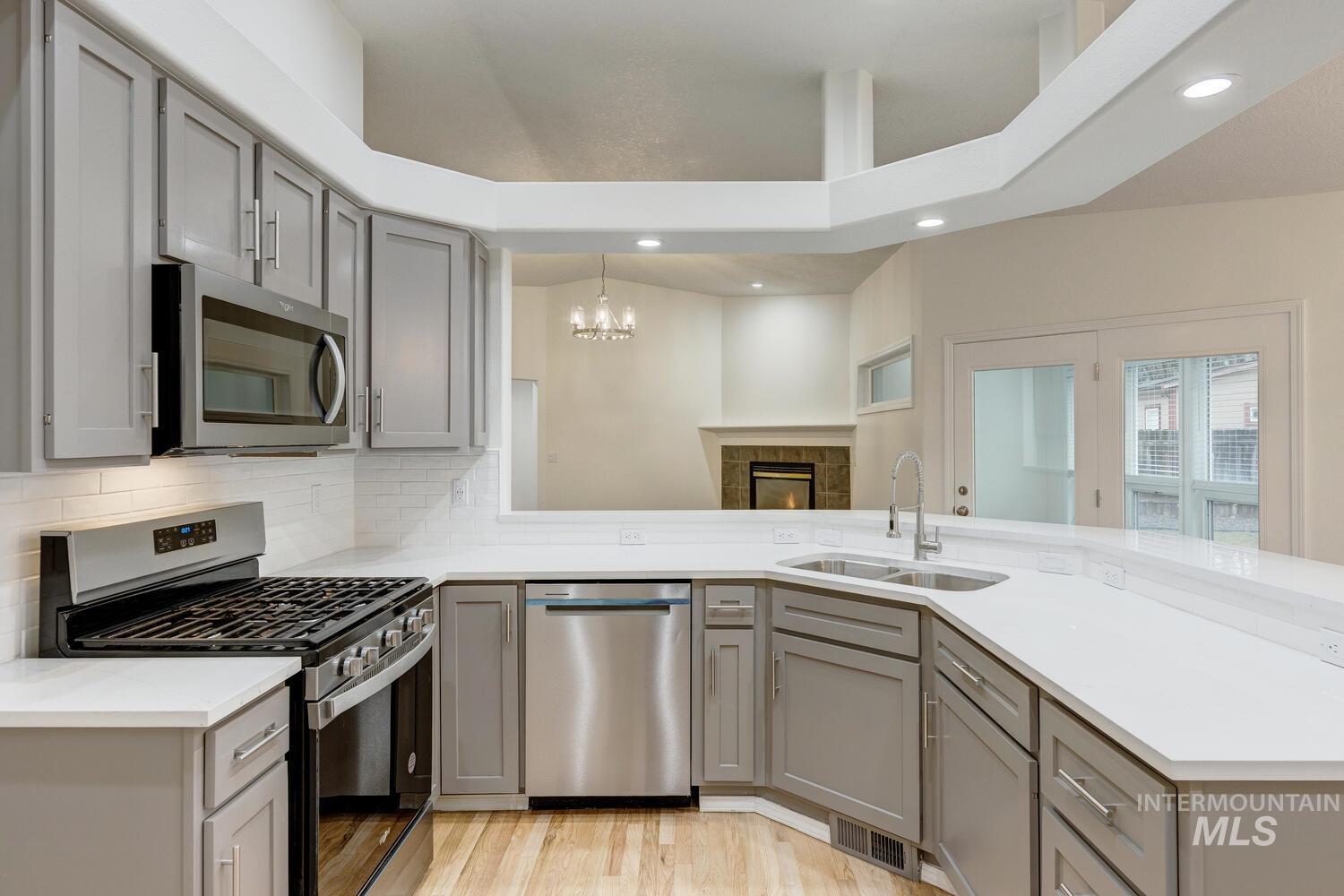 Kitchen featuring gray cabinetry, appliances with stainless steel finishes, a chandelier, a peninsula, and light stone countertops