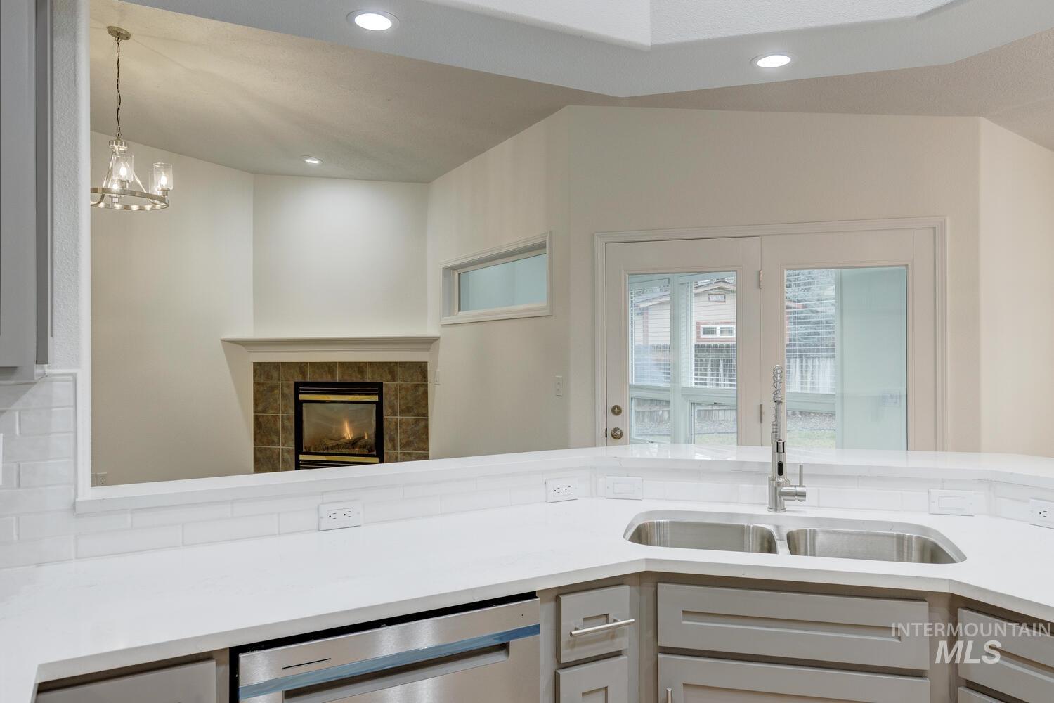 Kitchen with light stone counters, stainless steel dishwasher, a tile fireplace, hanging light fixtures, and recessed lighting